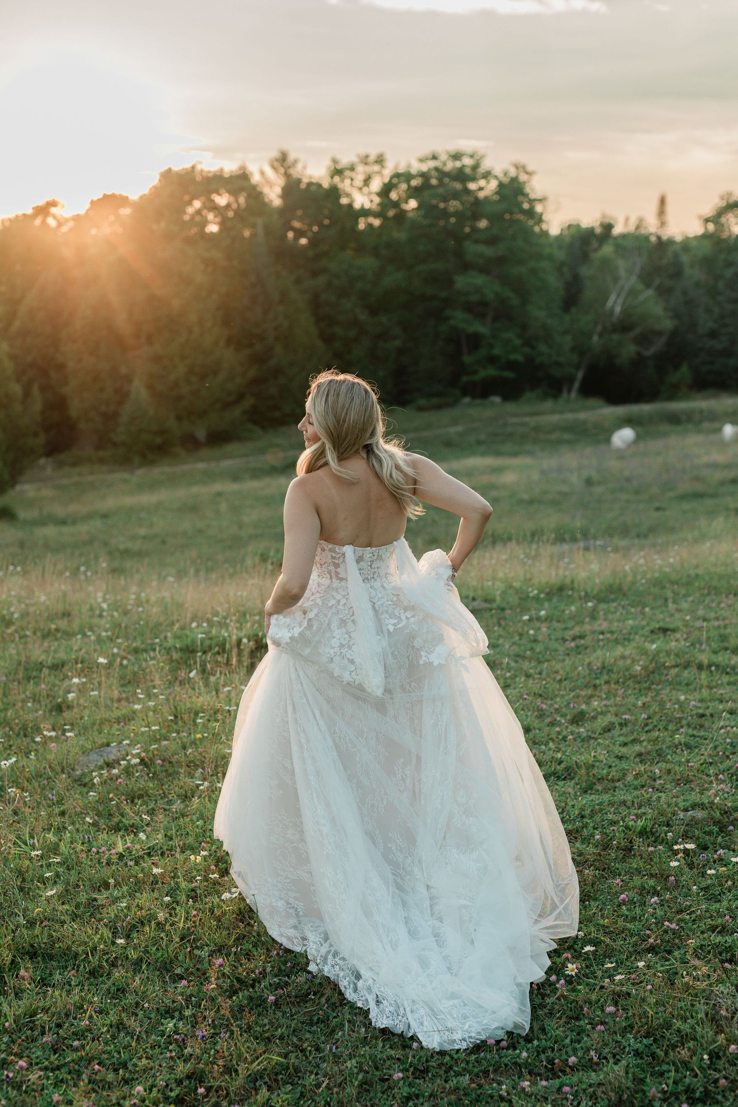 A person in a flowing white lace wedding dress runs through a sunlit meadow at golden hour.
