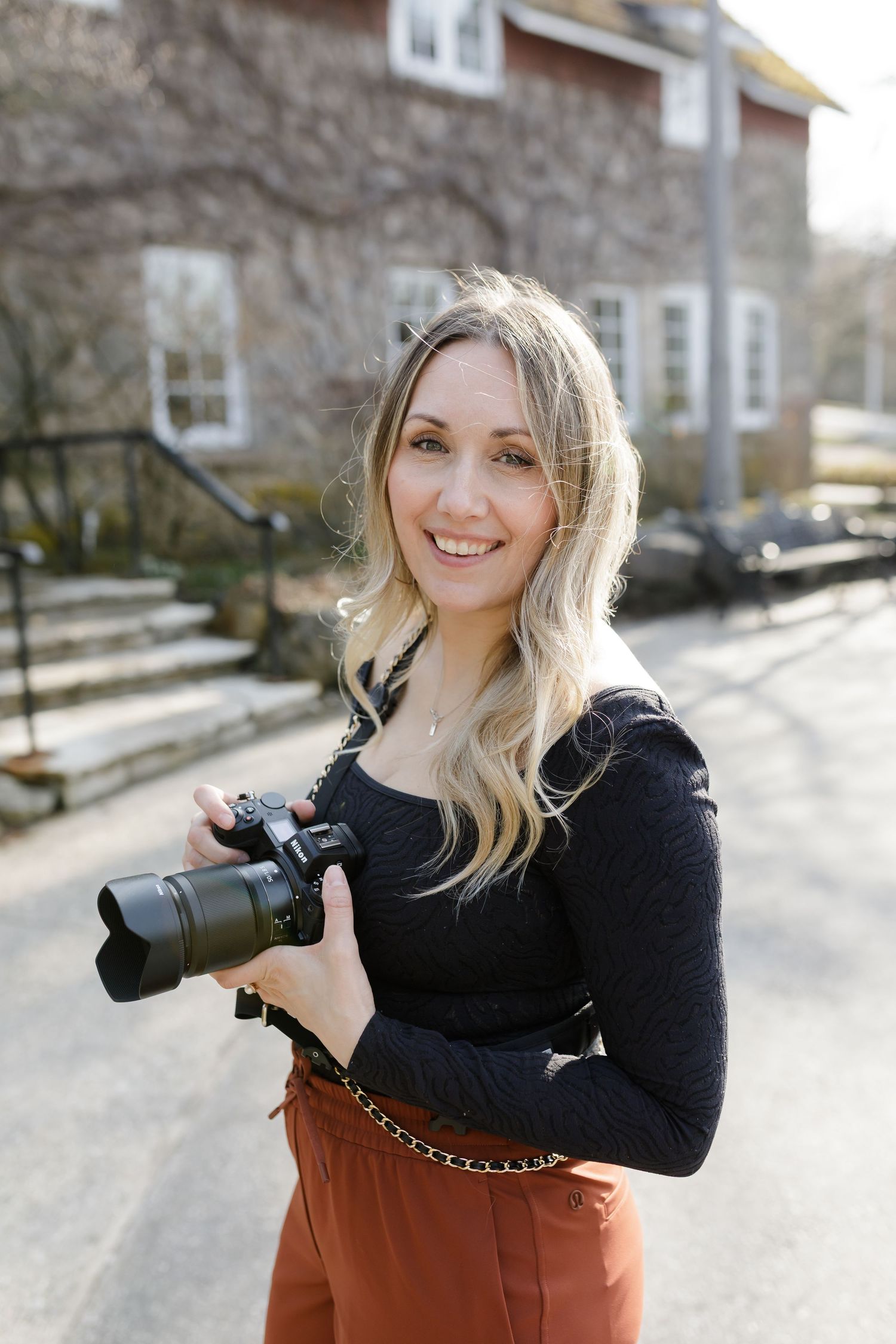 Professional photographer Destiny Dawn i holding camera outdoors on sunny winter day Ancaster Old Mill in Ancaster Ontario