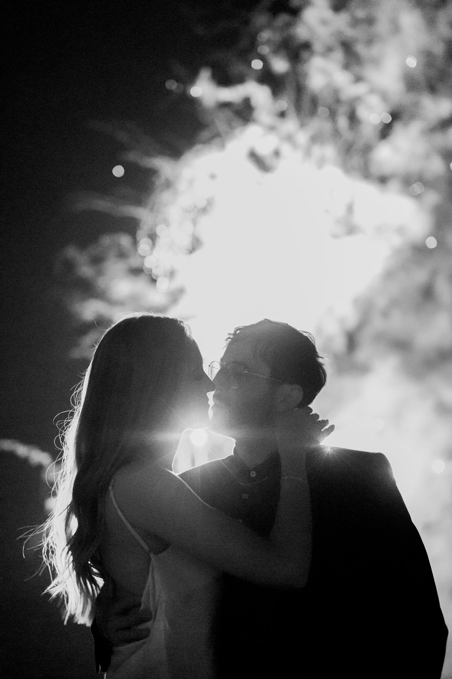 A romantic silhouette series of a couple kissing against bright backlighting in black and white photography.