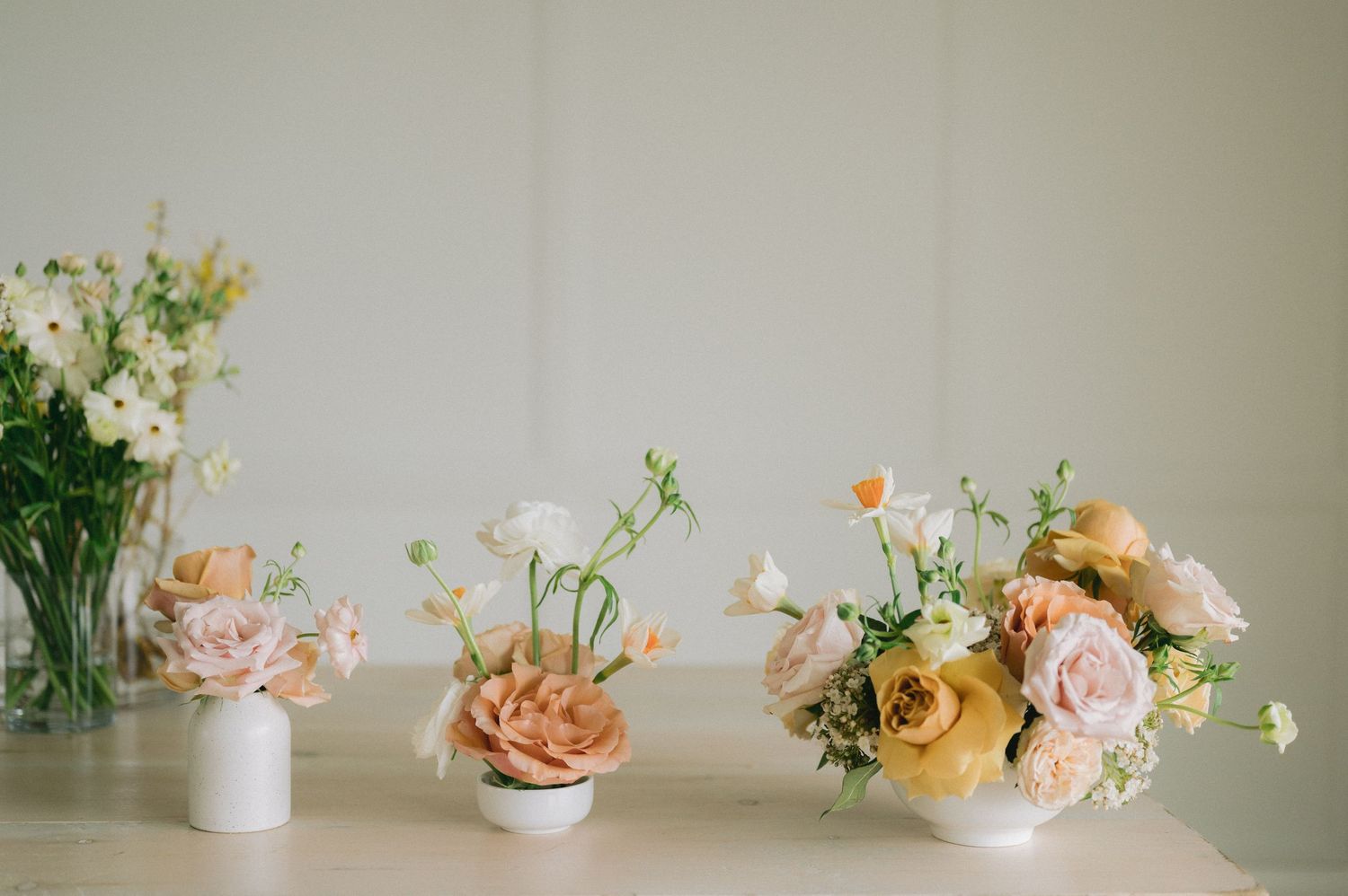 A series of delicate floral arrangements with pink roses and peach blooms in white vases against a light neutral background.