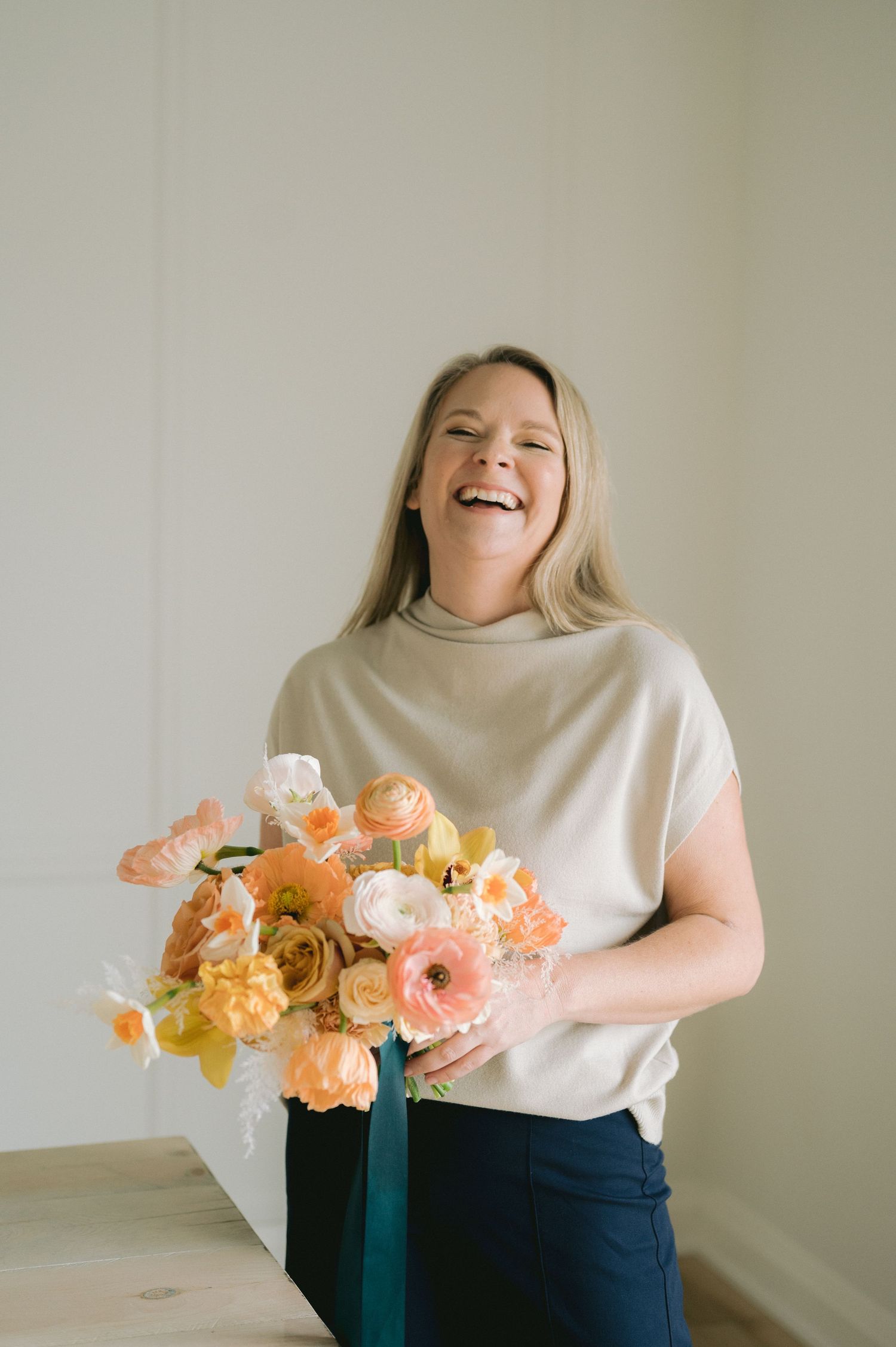 A series of photos showing a person in a white top holding colorful peach and coral flowers against a neutral wall.