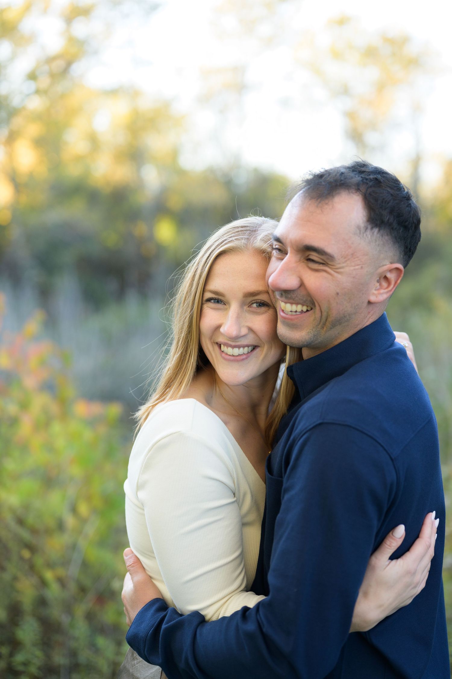 A couple shares tender moments outdoors in a natural setting during golden hour while wearing navy and cream colored outfits.