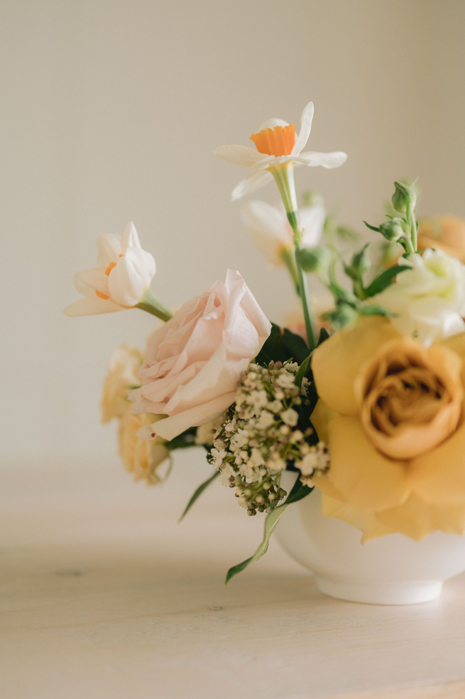 A soft, romantic arrangement of peach roses and white flowers in a delicate vase against a neutral background.