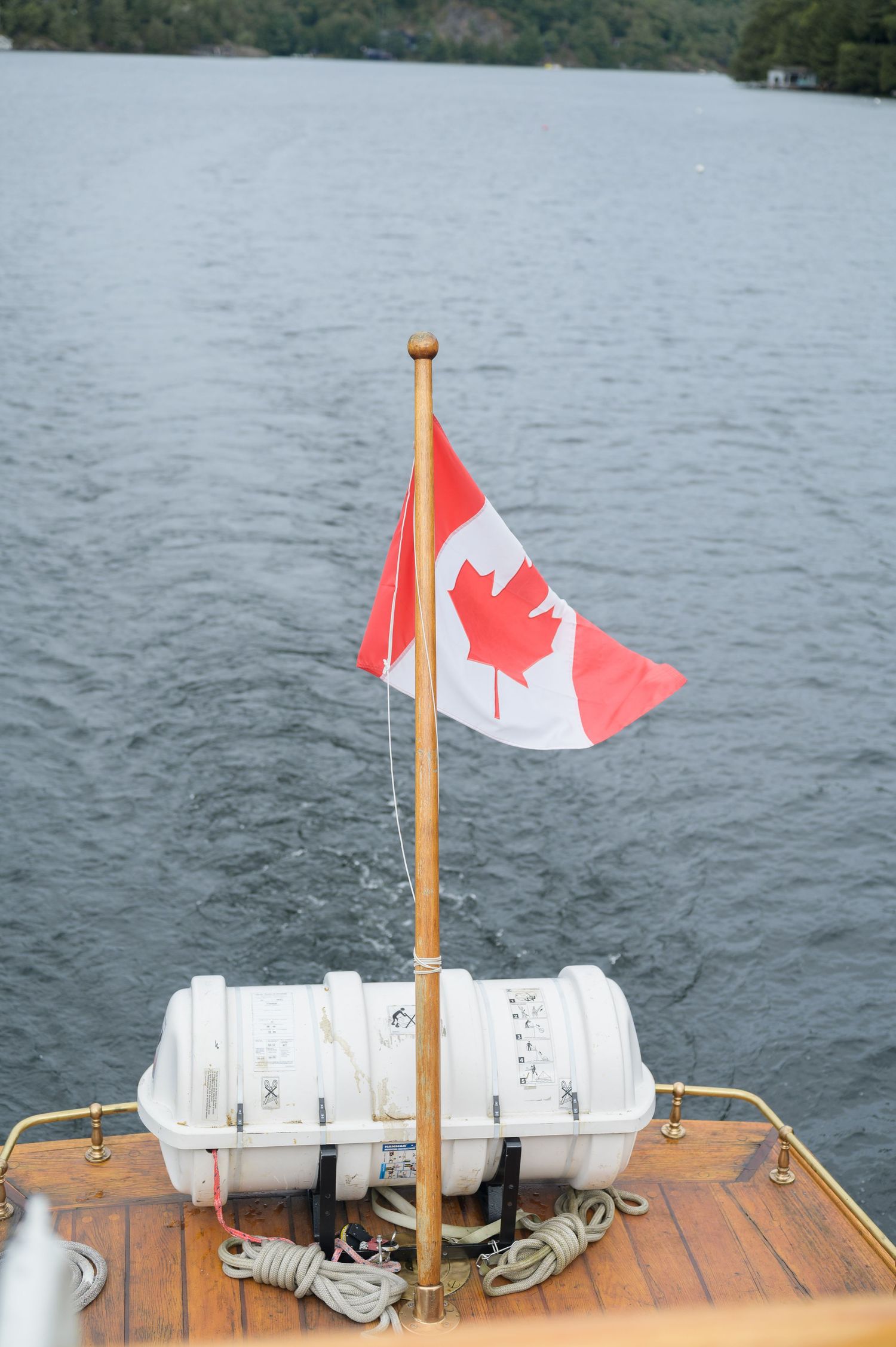 Canadian flag mounted on wooden boat deck with lake and trees in background.