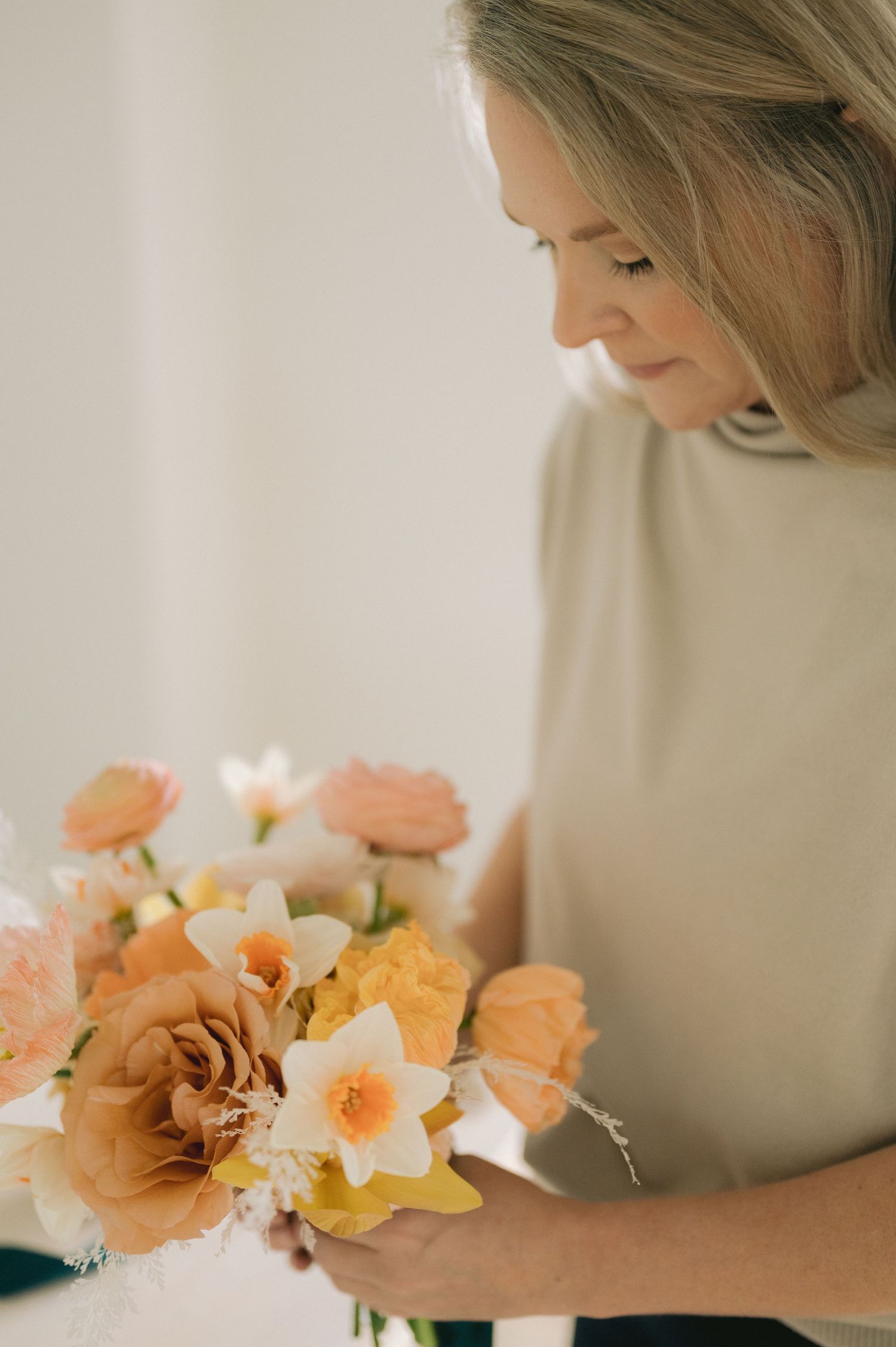 A florist carefully arranges delicate peach and coral colored flowers in a soft, natural light setting.