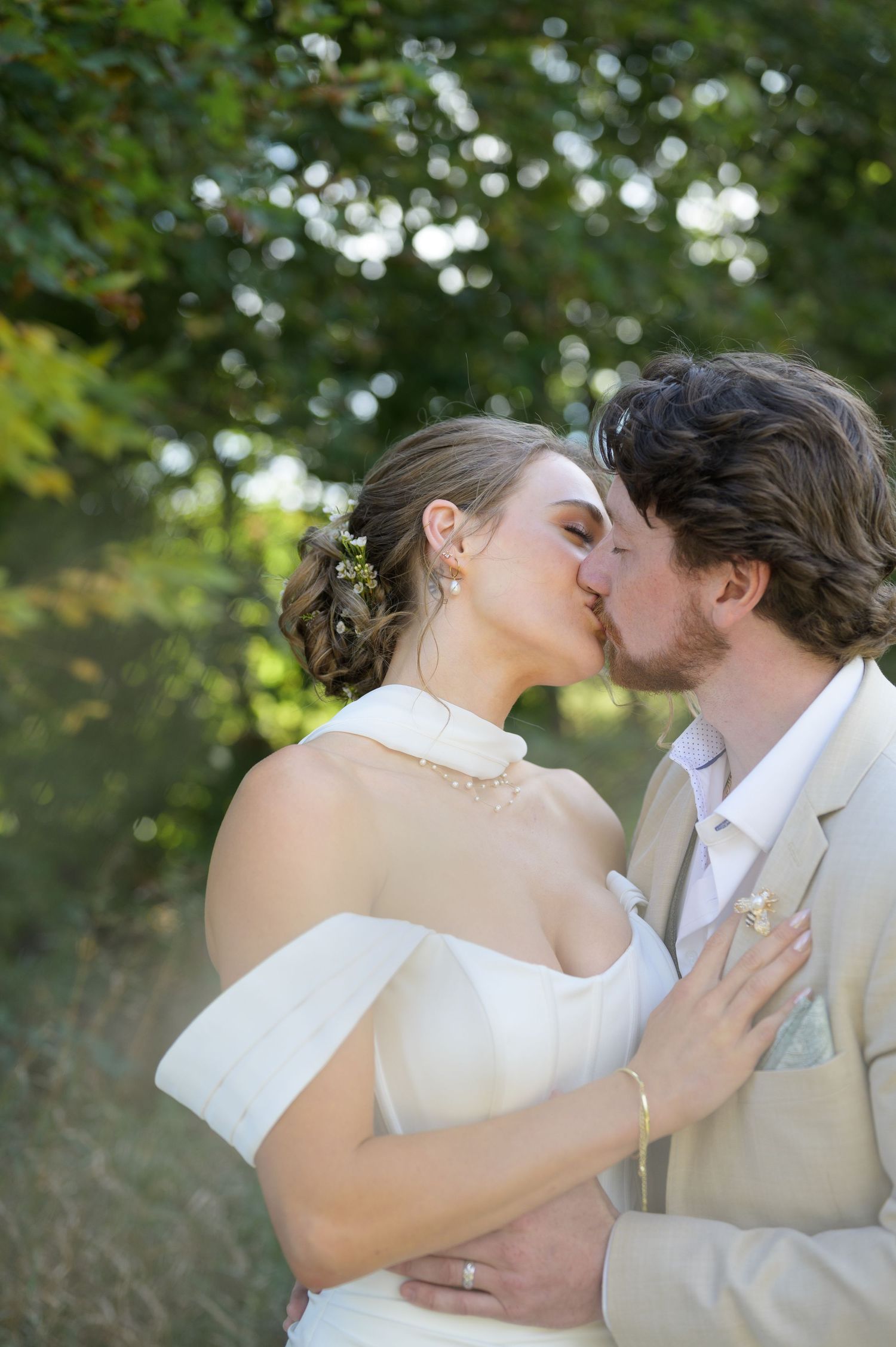 Intimate wedding kiss captured in a sun-dappled garden setting with bokeh lights in the background.