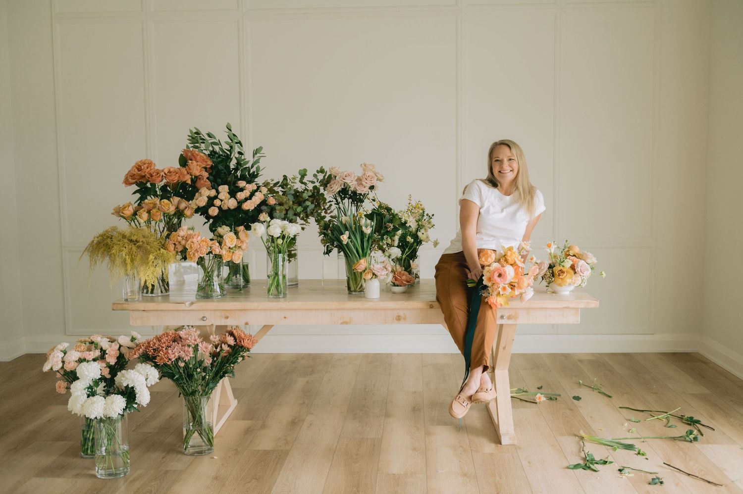 A series of floral arrangements in glass vases with peach and pink blooms displayed in a bright white studio space.