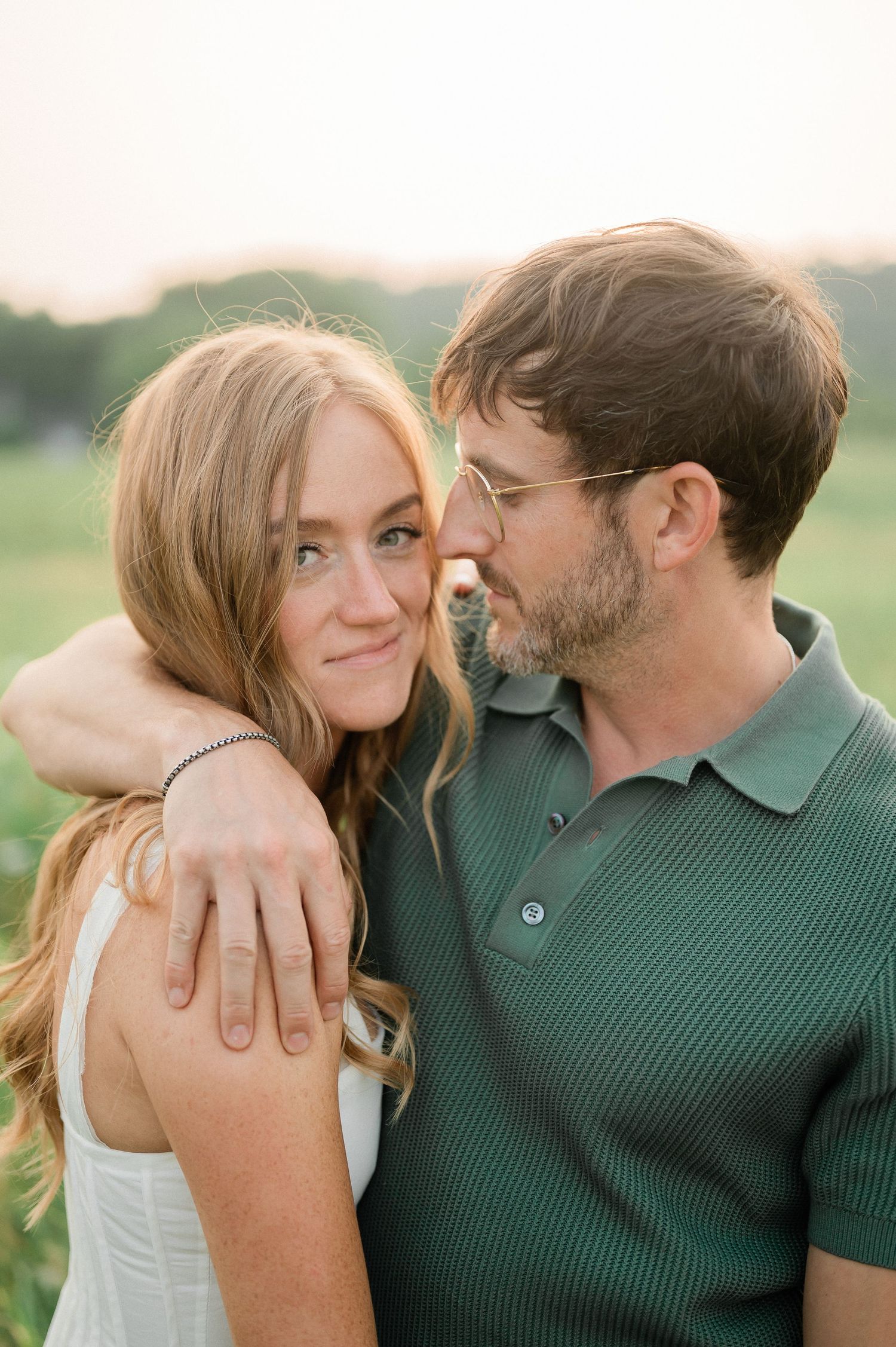 A romantic couple embraces outdoors in a field during golden hour, sharing an intimate moment together.