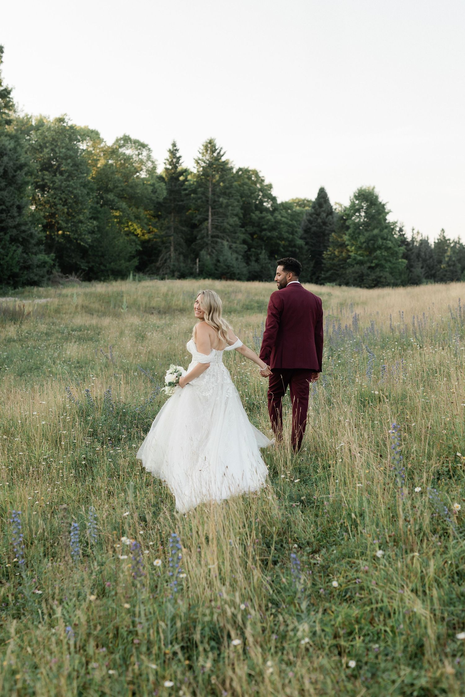 A couple in wedding attire walks through a serene meadow filled with wildflowers on their special day.