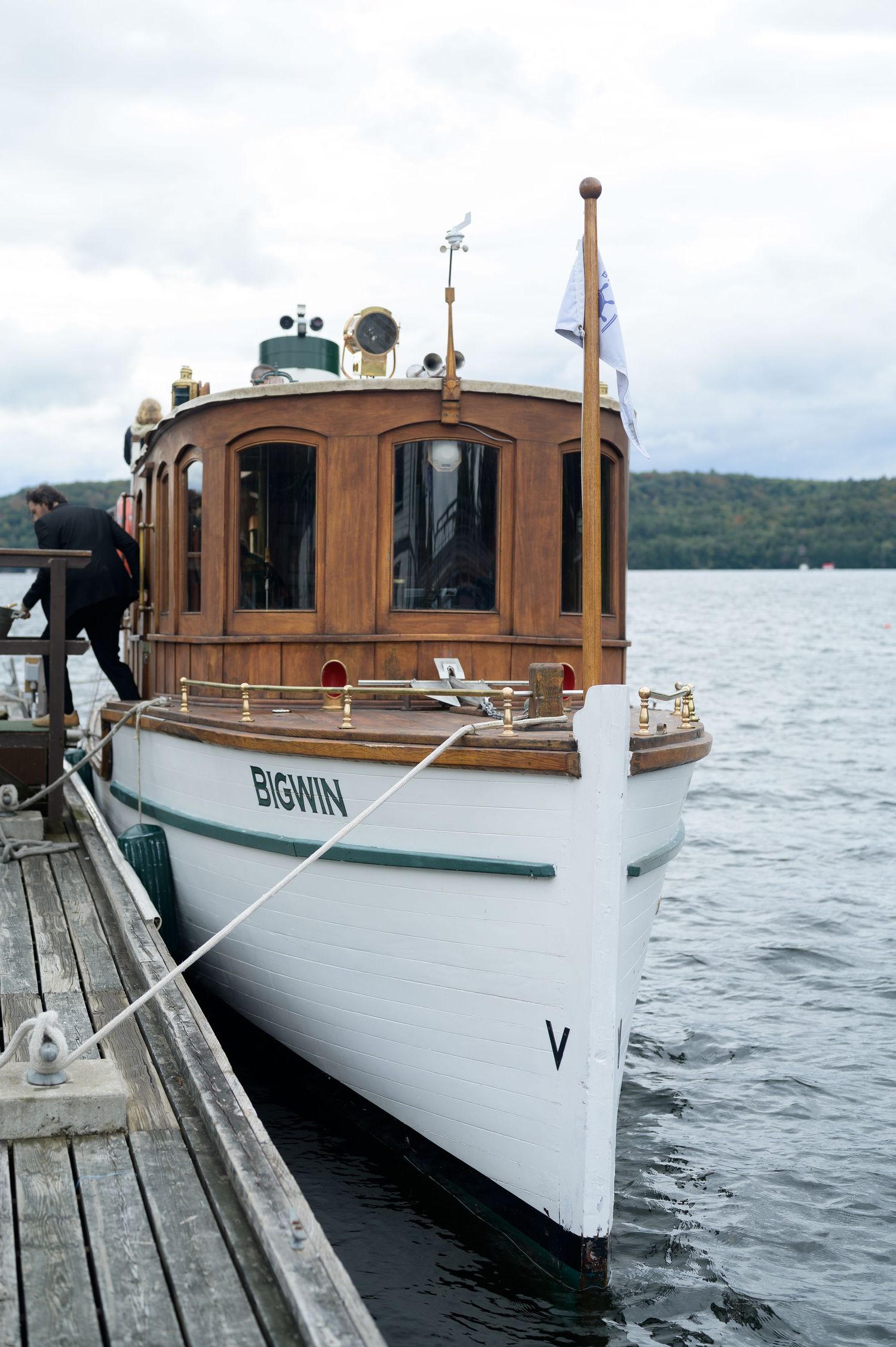 Classic wooden boat with white hull and brown cabin moored at dock on a cloudy lake day.
