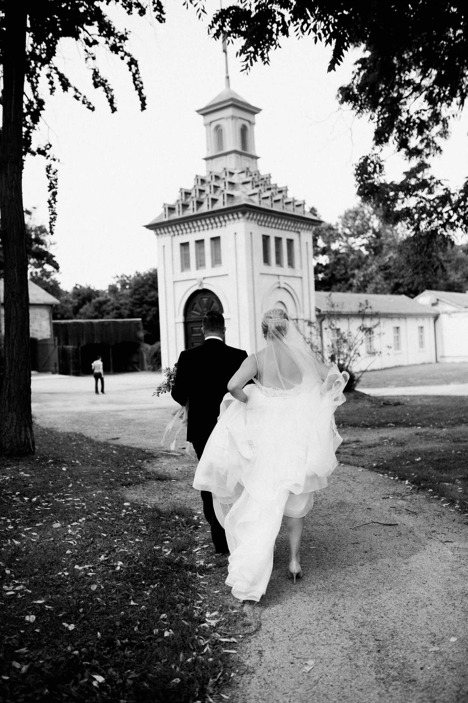Black and white series of a bride in a flowing white dress running along a garden path with classical architecture.