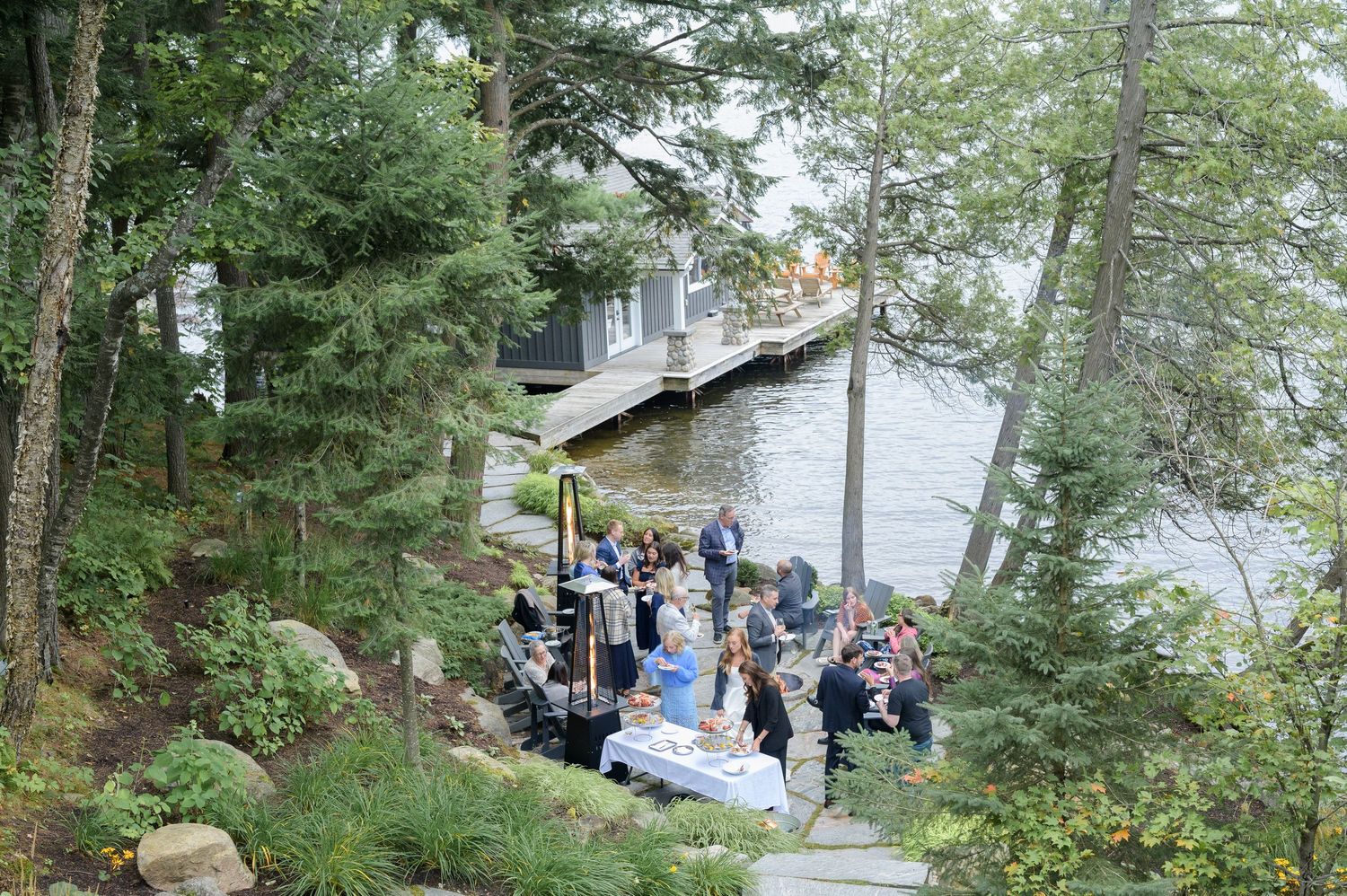 Scenic waterfront in Muskoka path through evergreen trees with people walking along a wooden boardwalk by the lake.