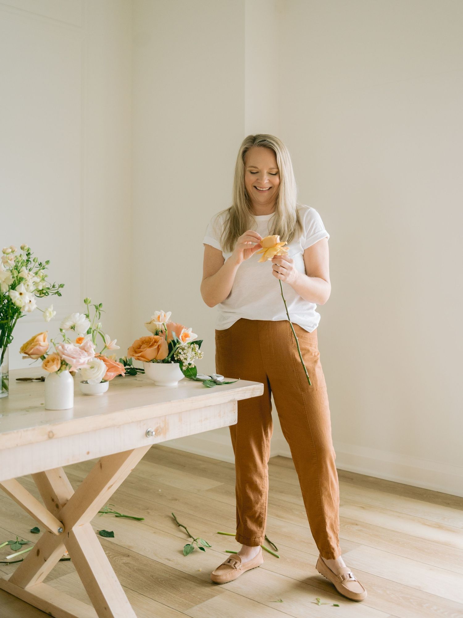 A series of lifestyle photos showing someone arranging flowers in a white vase on a light wooden table.