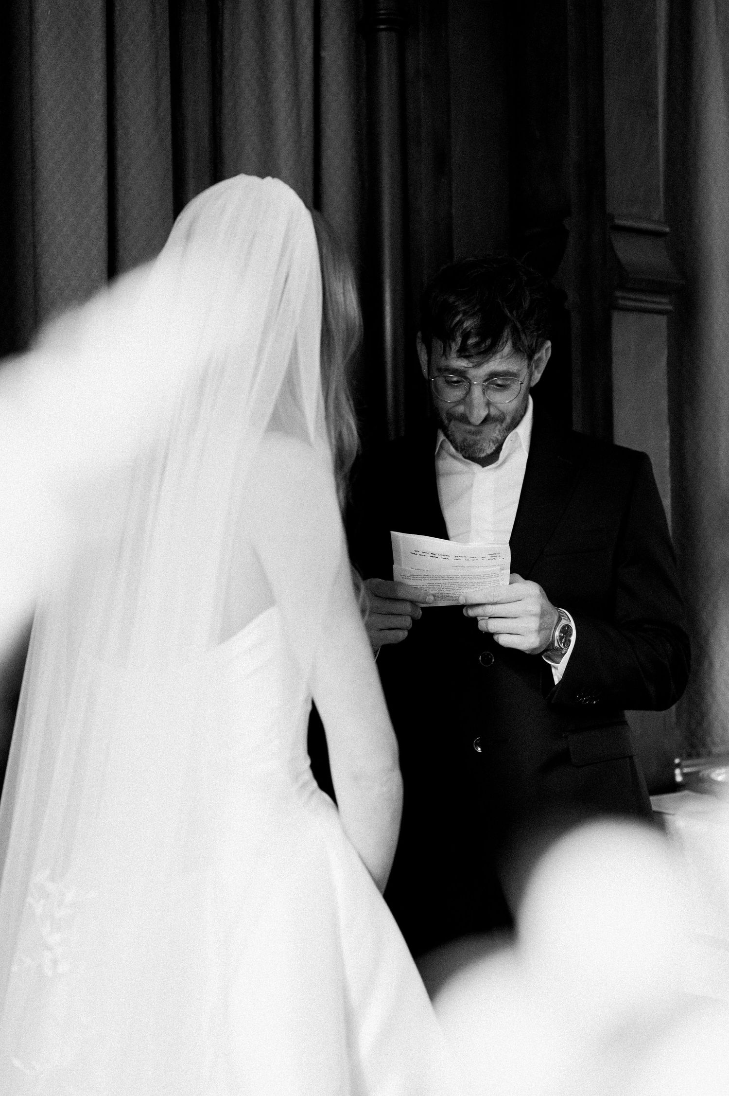 Black and white wedding ceremony photo showing bride in veil and guests in formal attire at church.