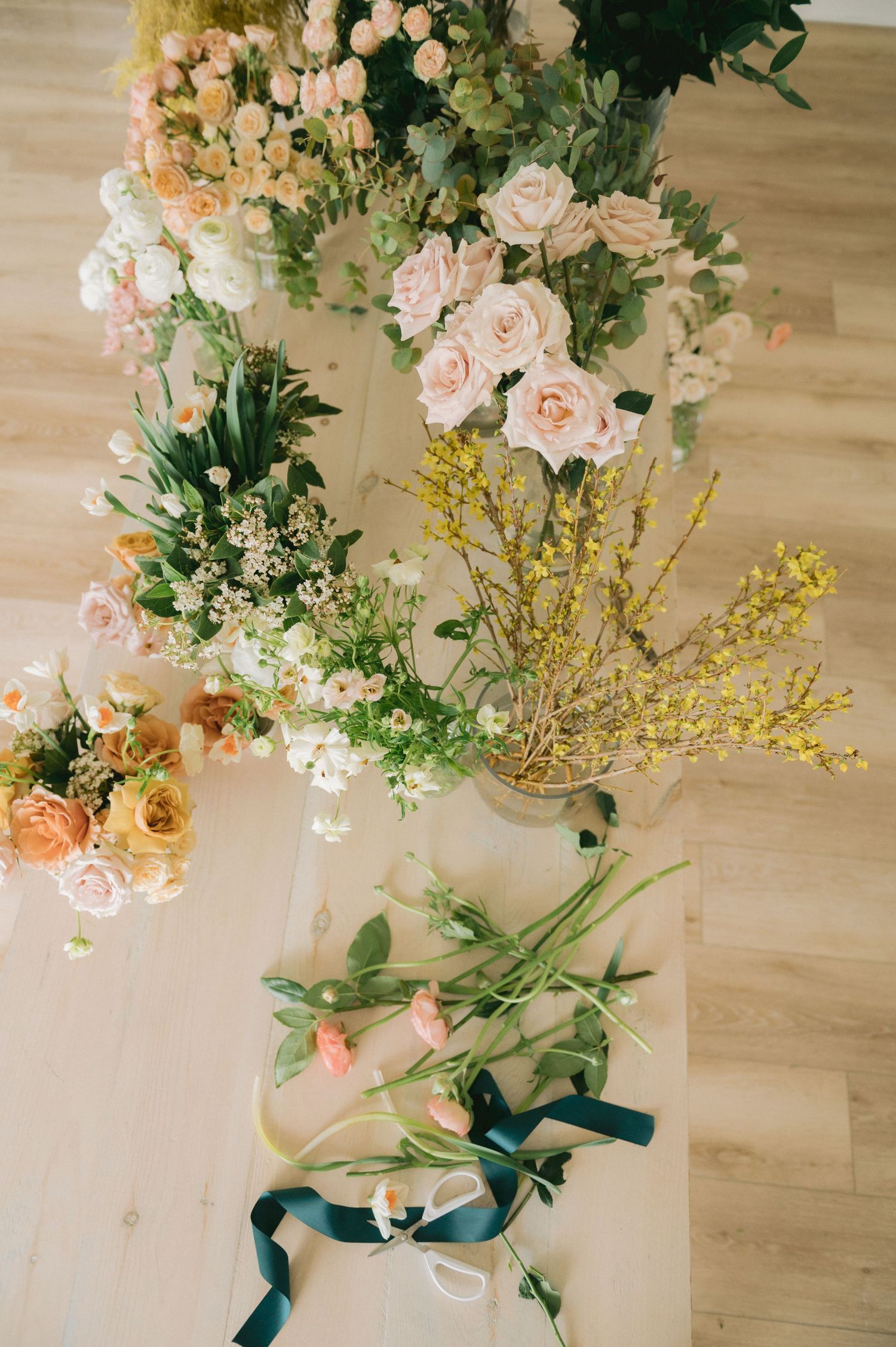 An overhead view of lush floral arrangements featuring pink roses, greenery, and yellow blooms on a wooden floor.