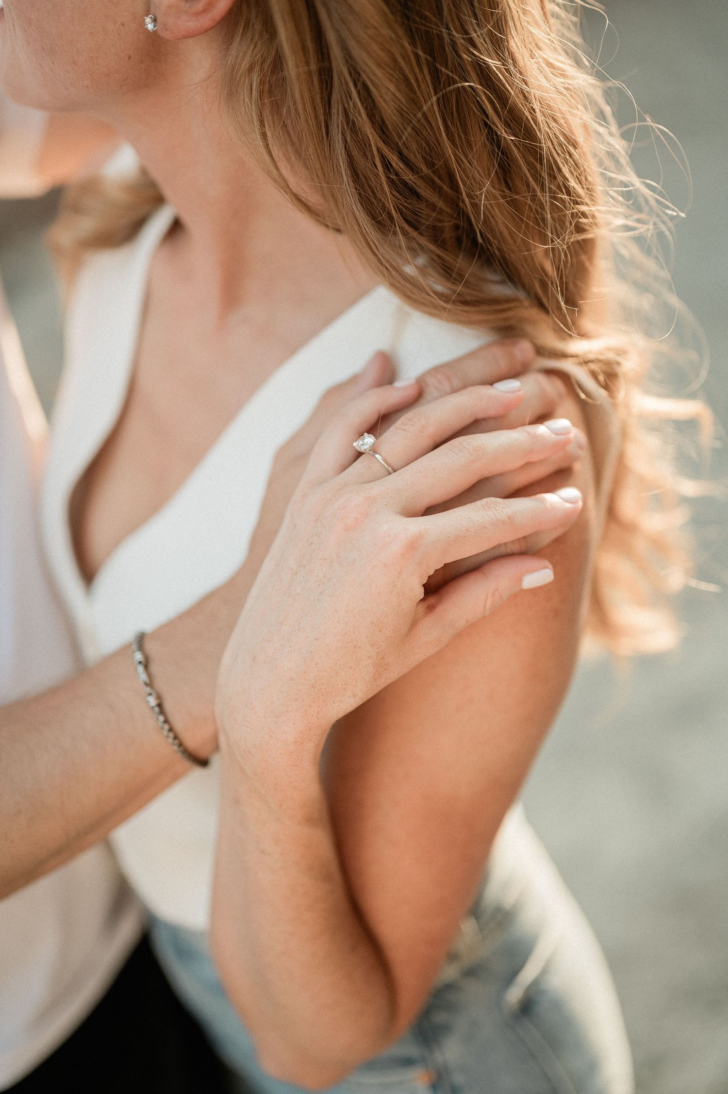 Close-up shot of hands displaying an engagement ring against a soft blurred background.