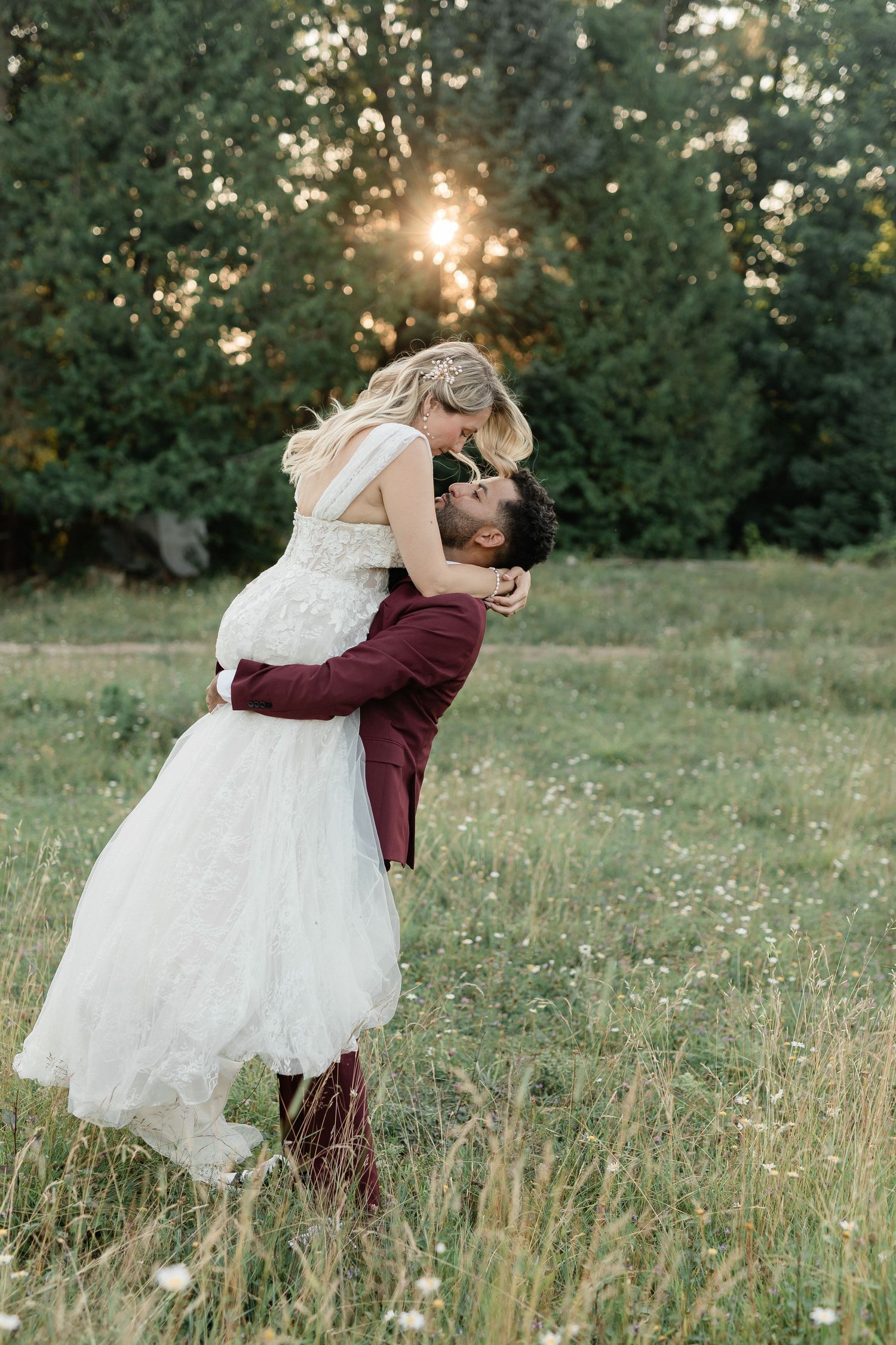 A romantic couple in wedding attire embrace in a sunlit meadow with wildflowers during golden hour.