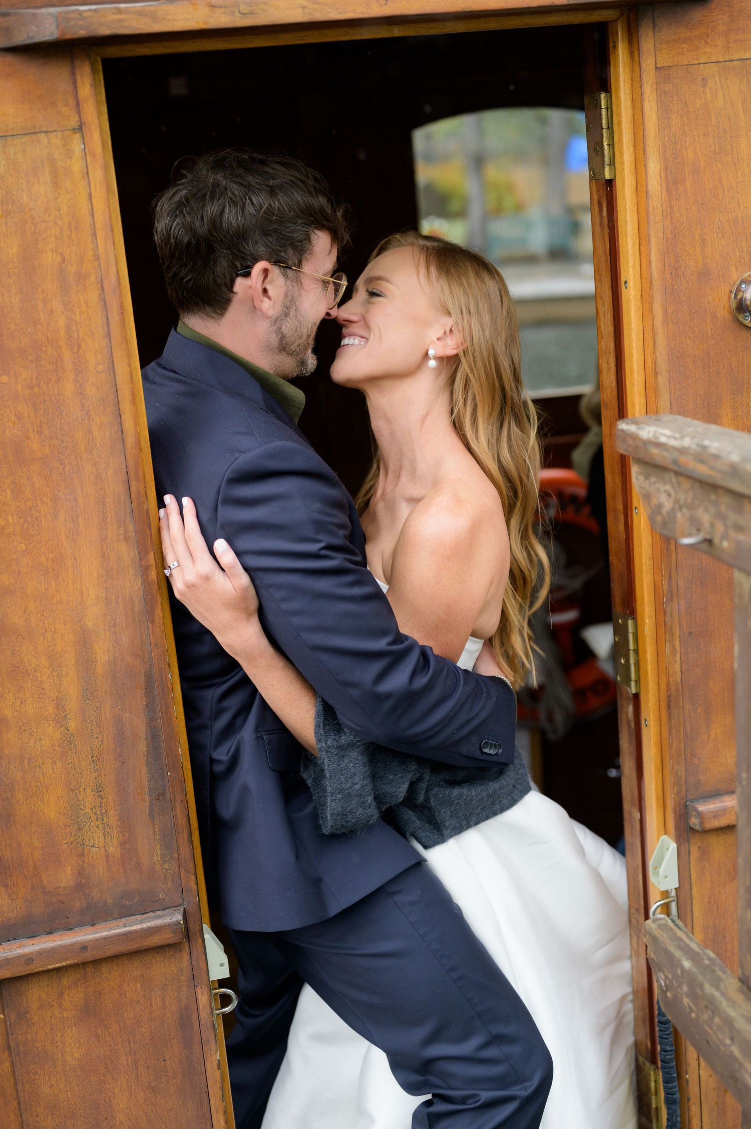 A couple in wedding attire share an intimate embrace against a rustic wooden doorway.