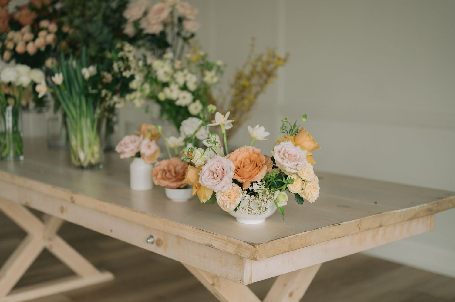 Rustic wooden tray filled with fresh flowers and decorative items on a light gray surface.