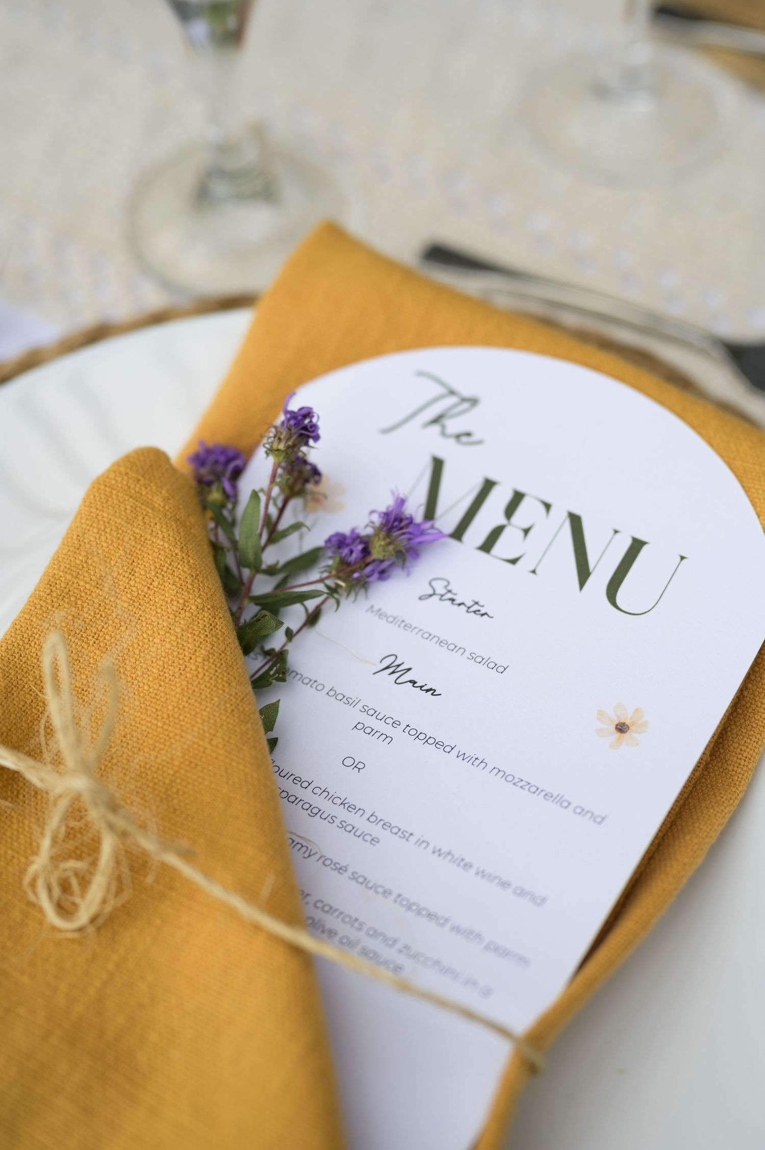 Wedding menu cards decorated with purple flowers and twine on golden napkins.