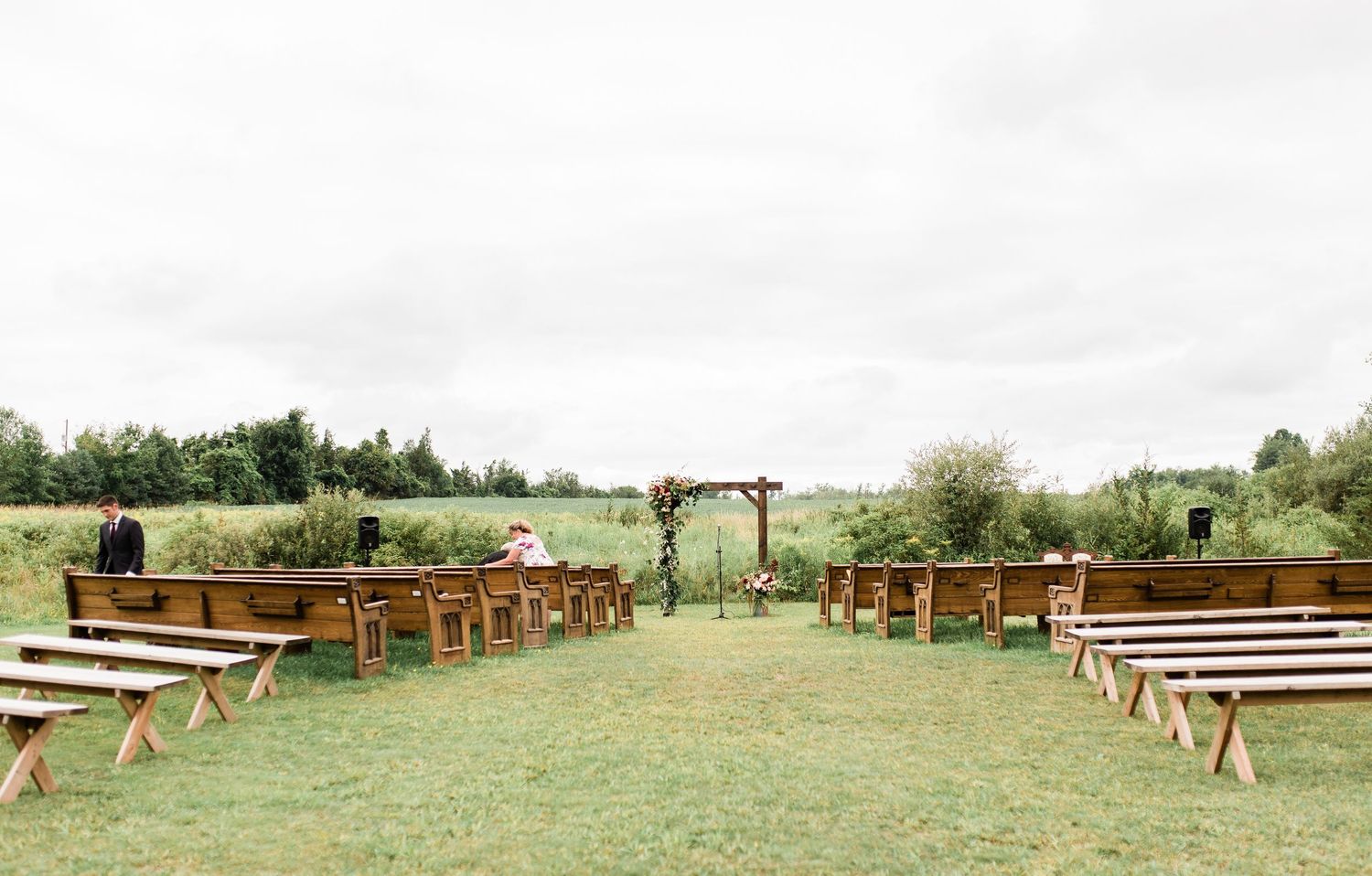 Rustic wooden benches arranged in rows on a grassy hillside for an outdoor wedding ceremony.