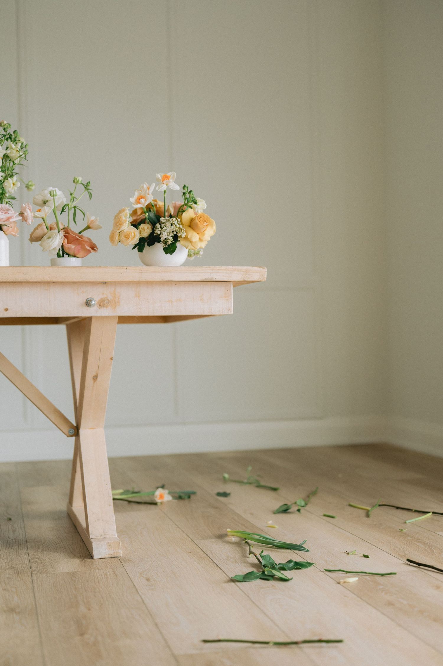 Wooden bench with peach-colored flowers and scattered greenery on light hardwood floor against white wall.