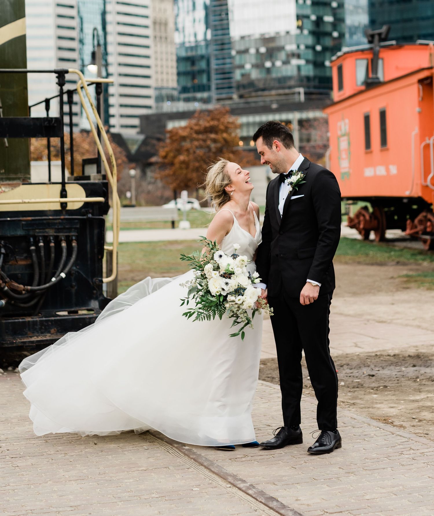 Bride and groom share a romantic moment on train tracks with urban buildings in the background.