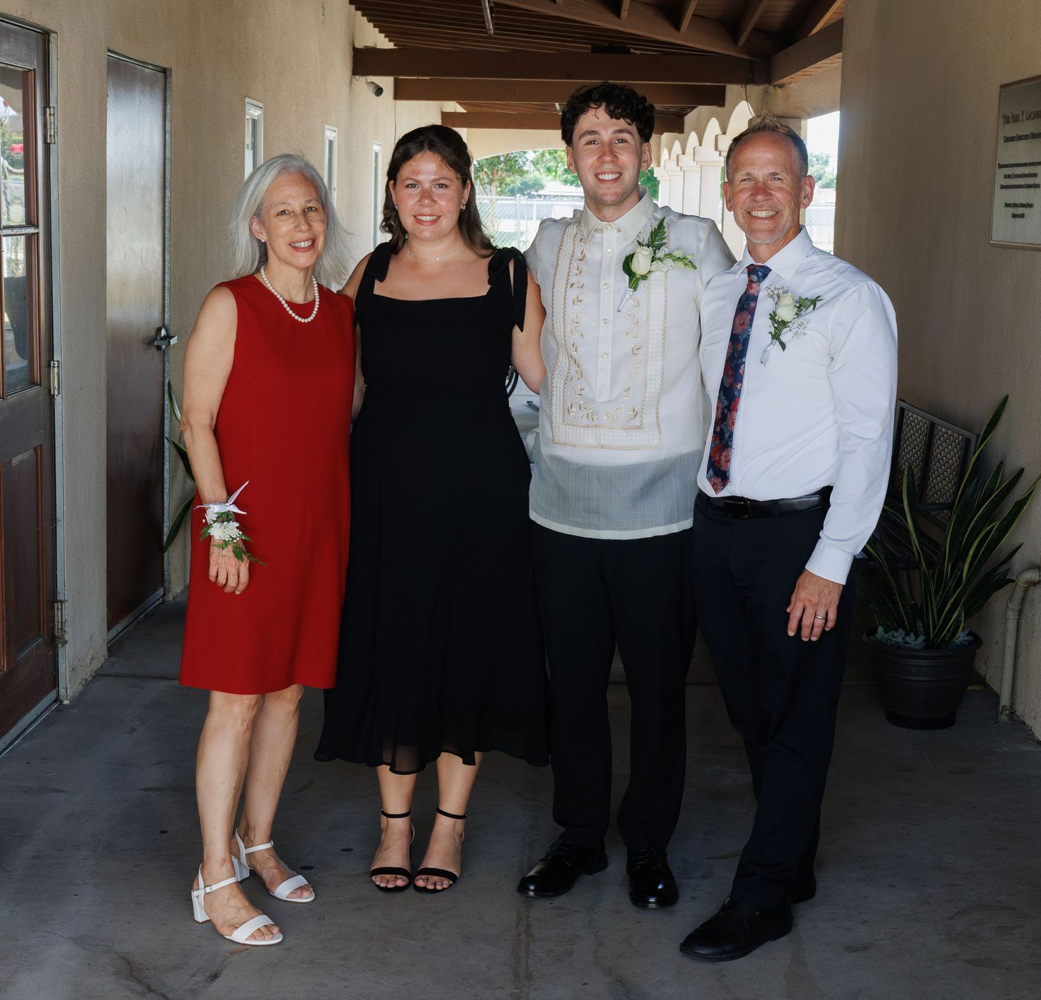 Family of four posing together dressed formally, smiling at a special occasion outdoors.