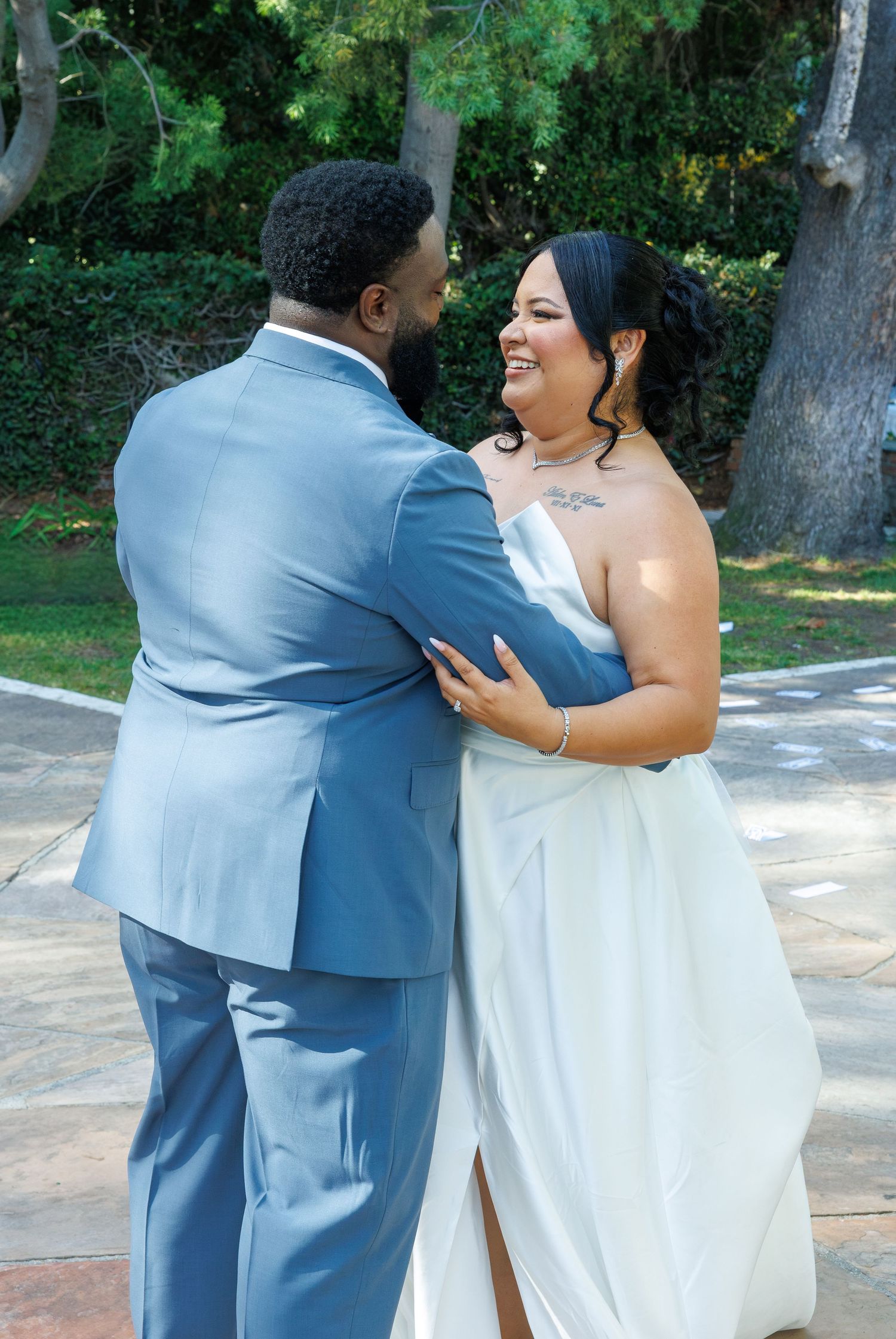 Bride in strapless white gown laughing with groom in blue suit during outdoor wedding portraits.