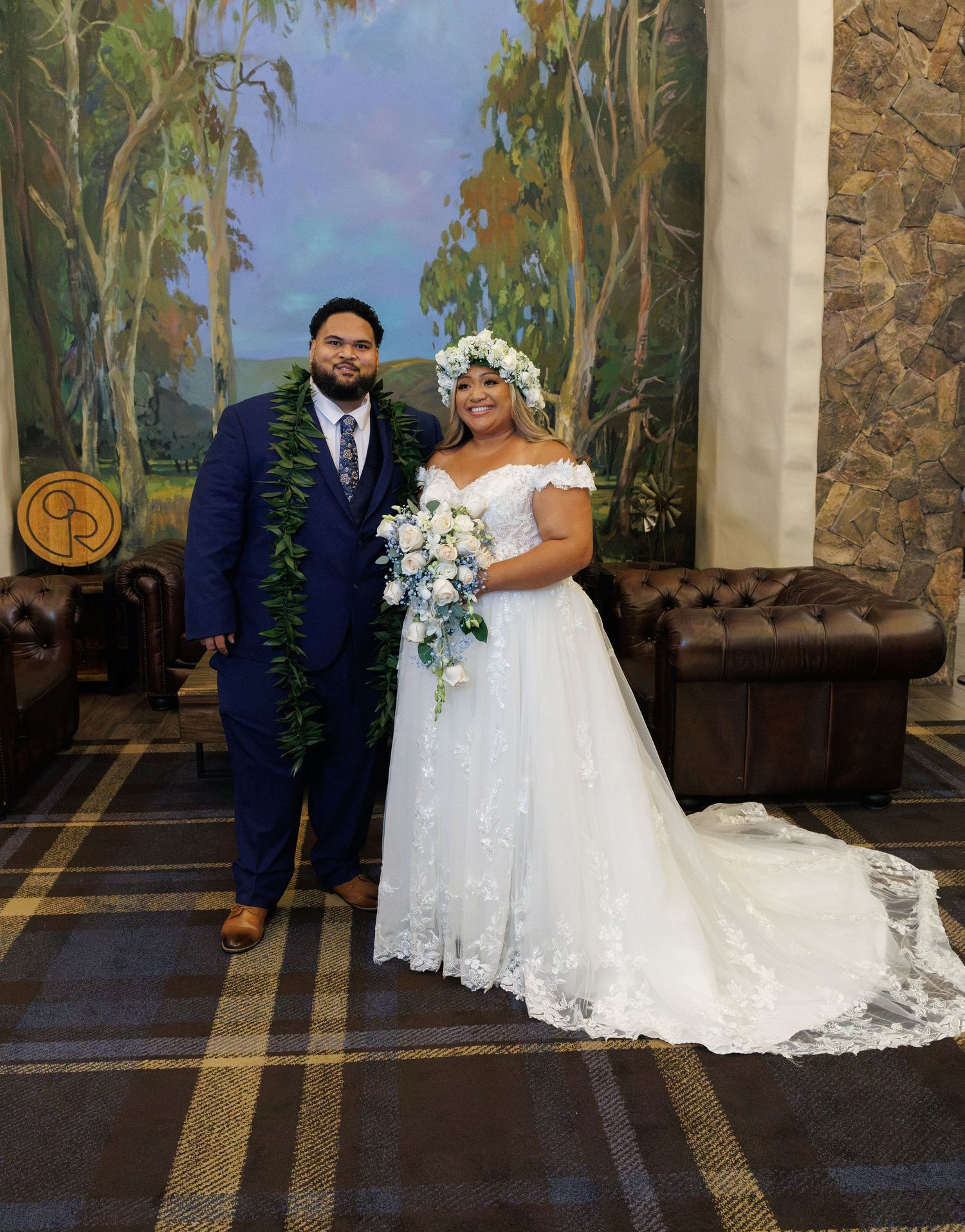 Bride in white lace ball gown and groom in navy suit with floral lei pose together at elegant wedding venue.