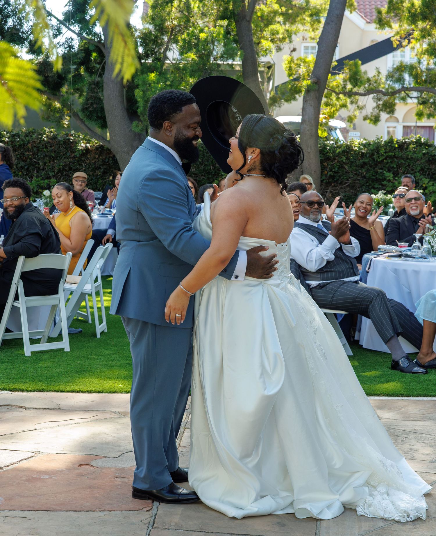 Bride and groom share first dance at outdoor wedding with guests watching and cheering.