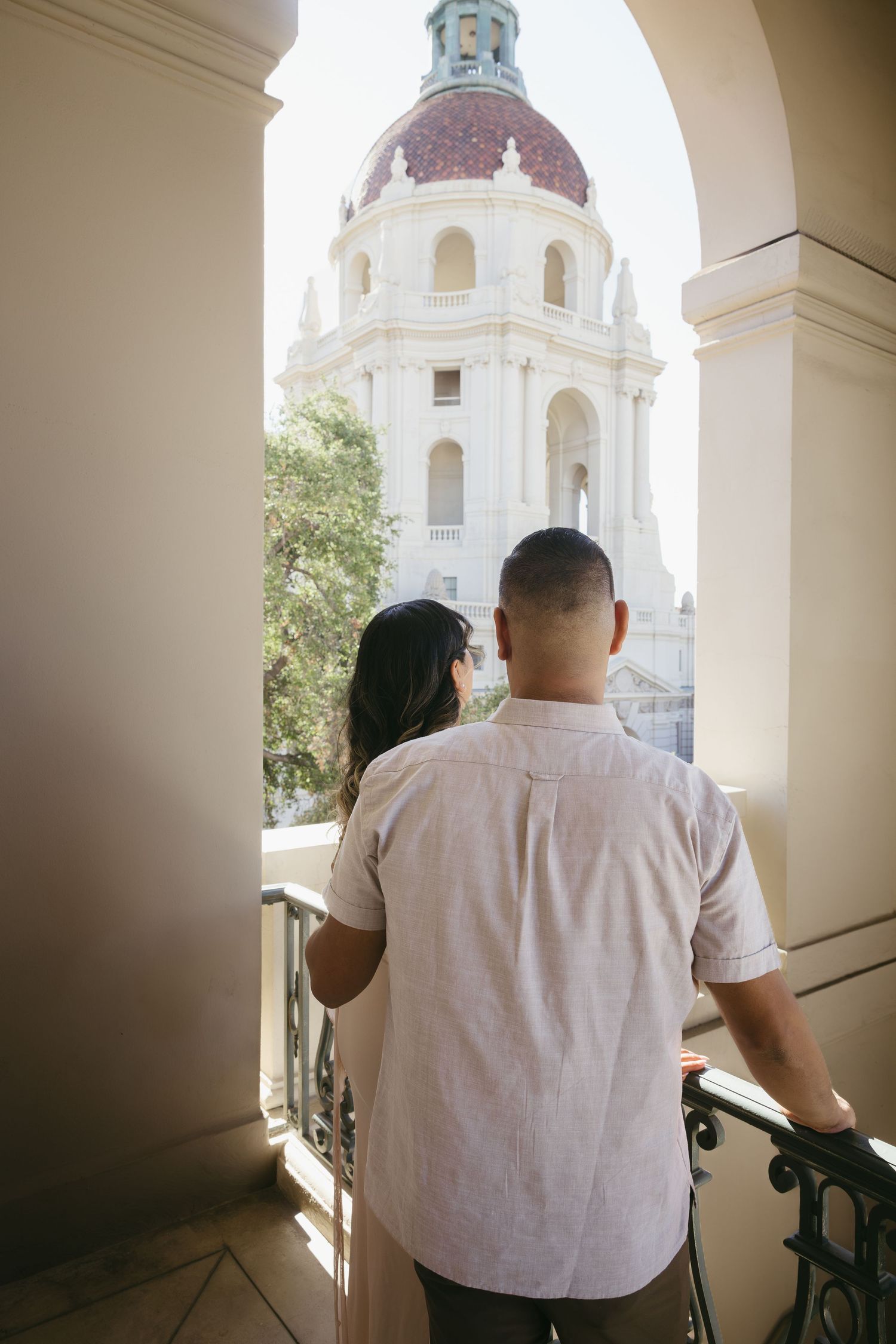Couple standing on a balcony admiring the historic Pasadena City Hall dome architecture.