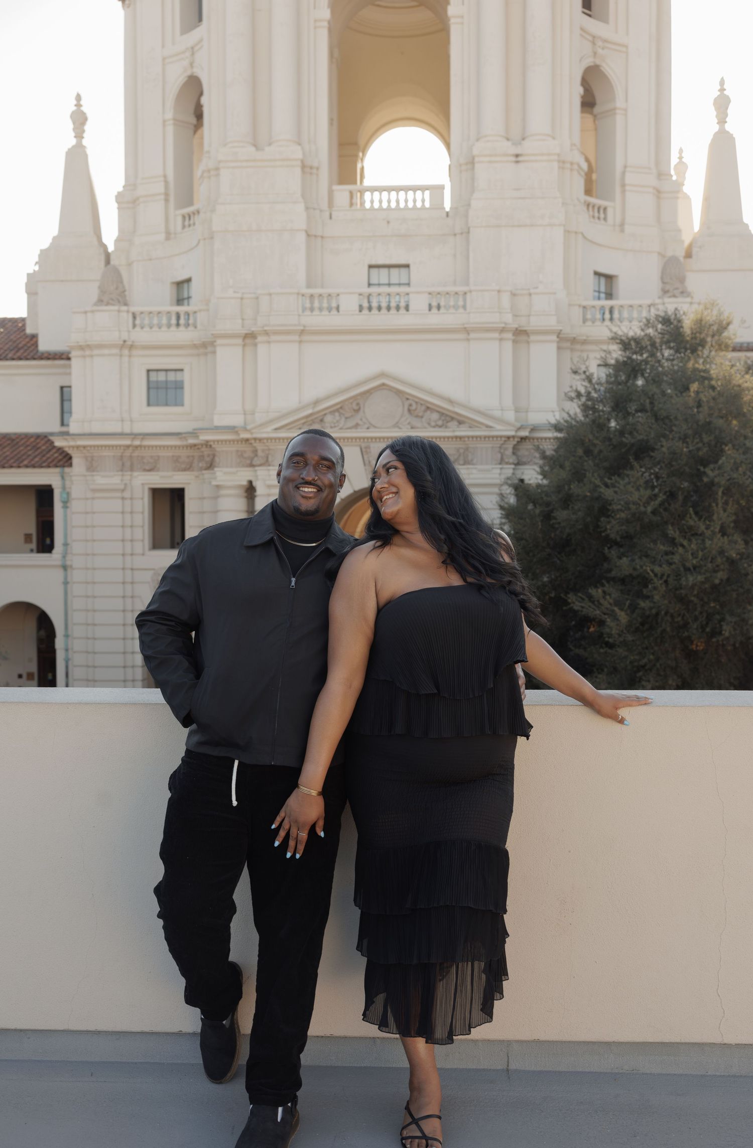 Couple in black outfits posing in front of a grand white building architecture.