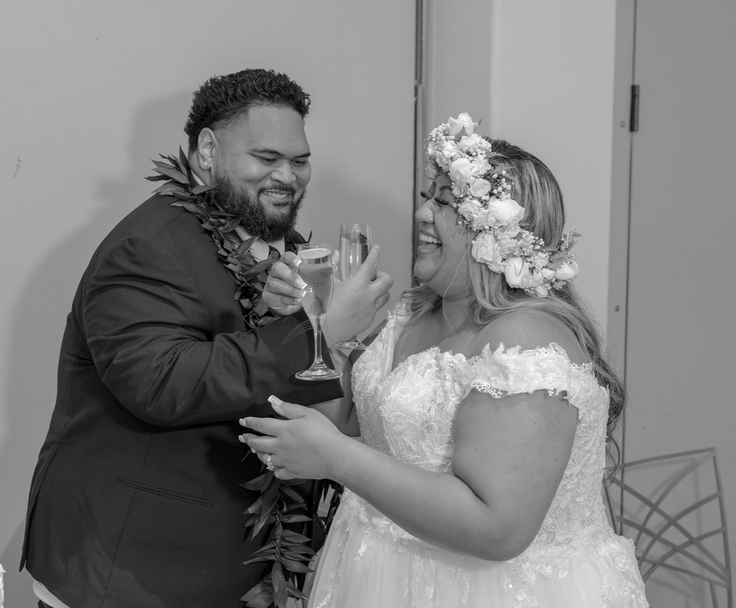 Black and white photo of a joyful bride and groom toasting with champagne glasses at their wedding celebration.