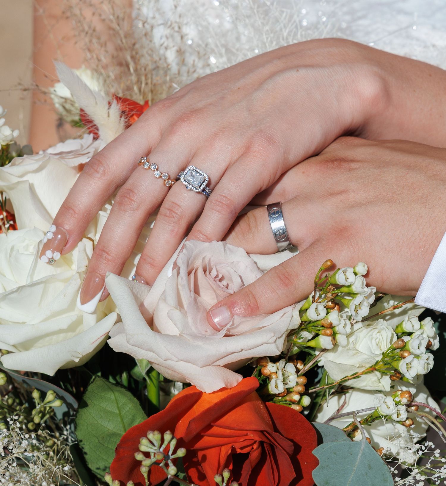 Close-up of newlyweds hands displaying wedding rings resting on a bouquet of white and red roses.