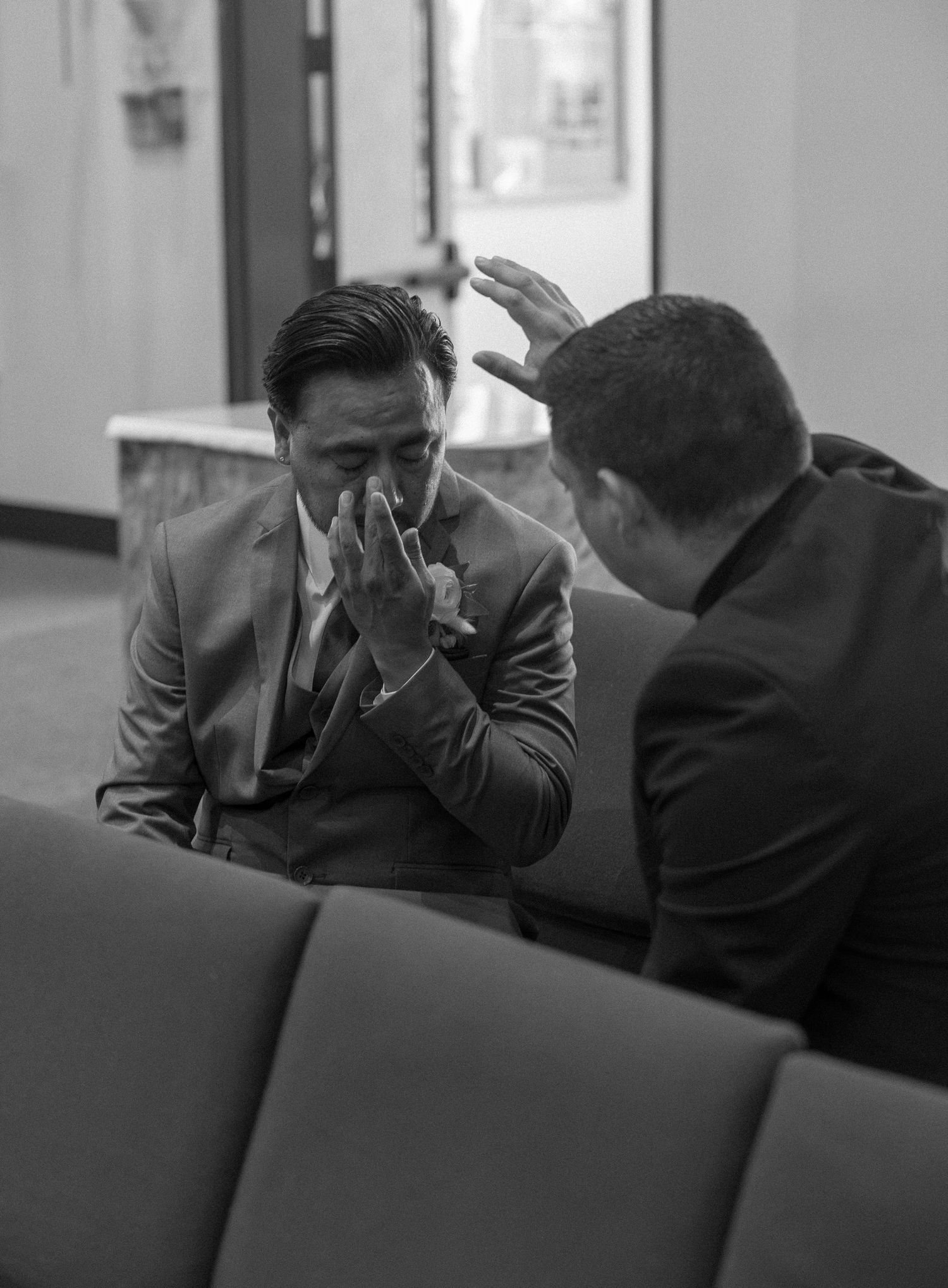 Black and white photo of a man in a suit wiping his tears as another man places a hand over his head in prayer.