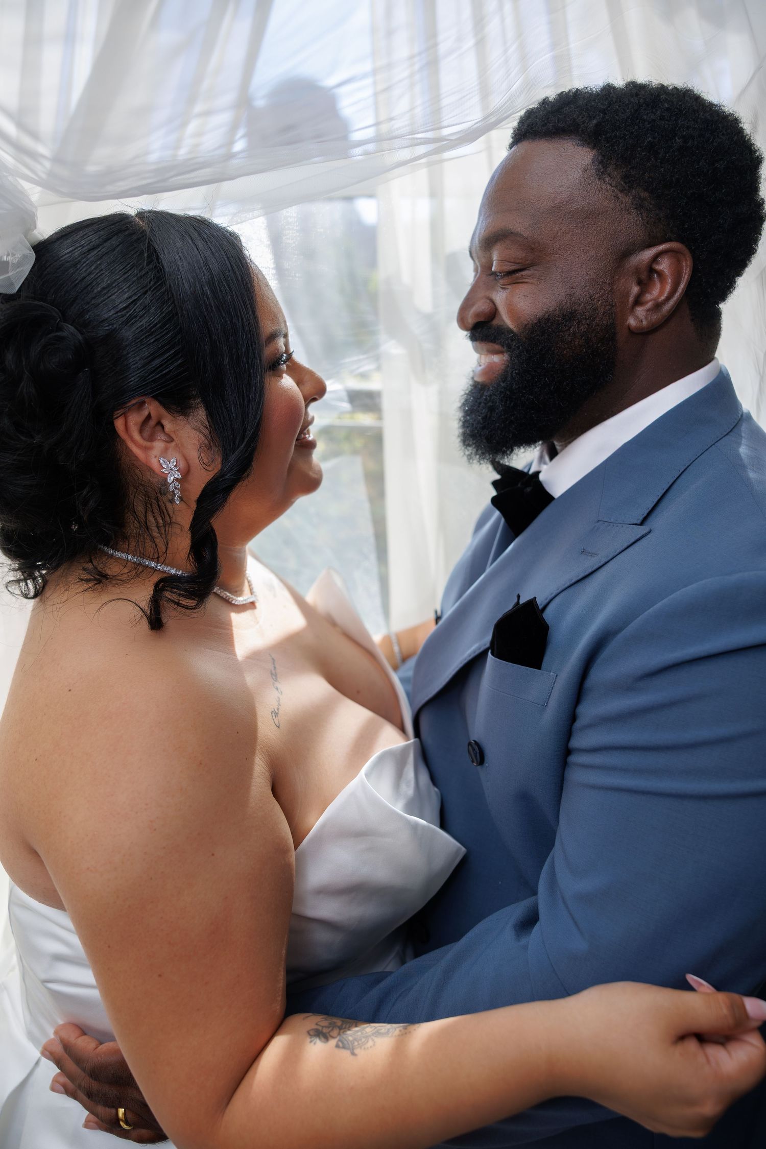 Bride and groom embracing and smiling at each other during wedding day first look indoors.