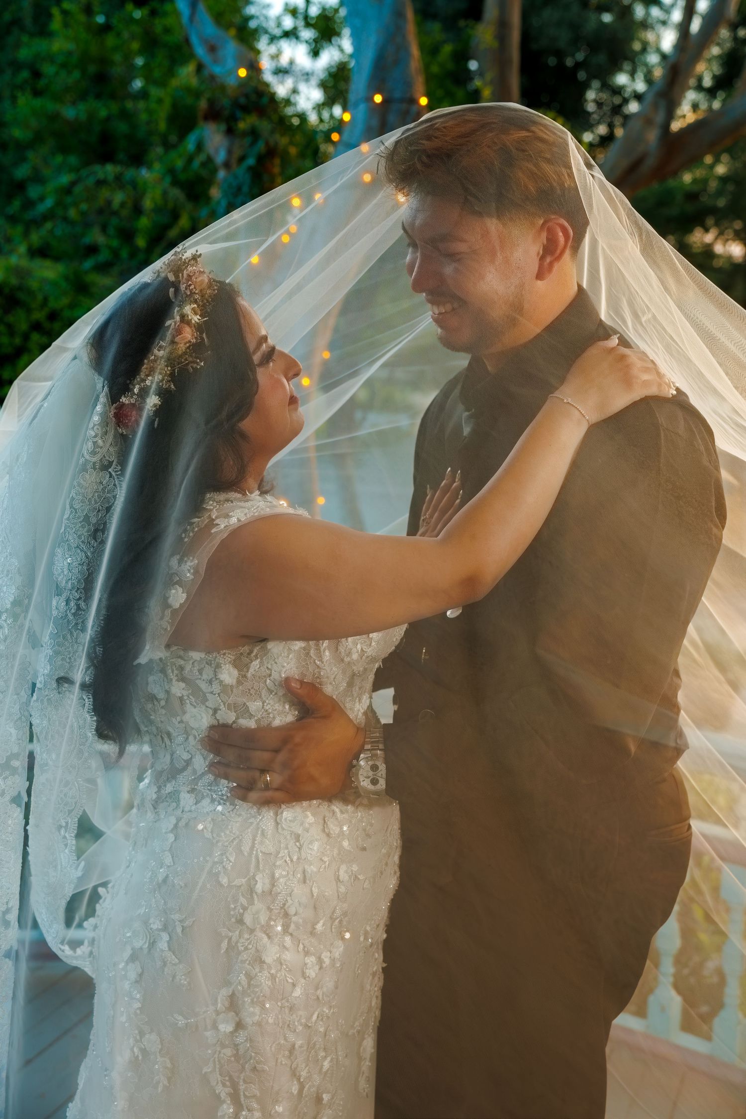 Bride and groom share a romantic moment under a flowing veil at an outdoor wedding ceremony.
