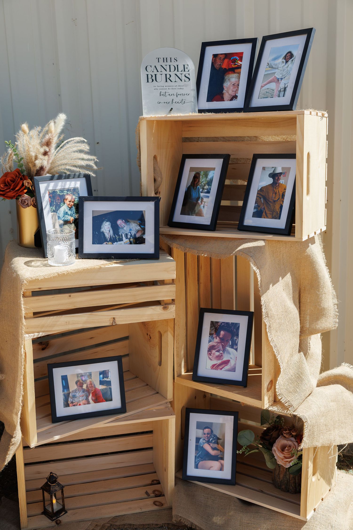 Rustic wedding memorial display with framed photos arranged on stacked wooden crates with flowers.