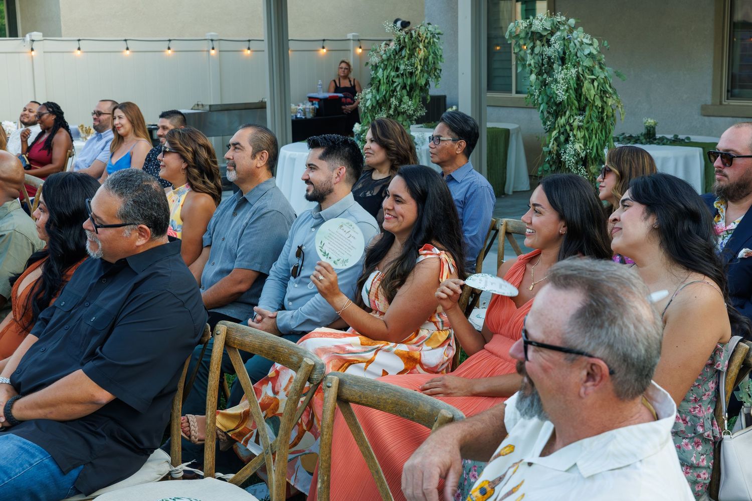 Diverse group of smiling adults seated outdoors at an evening event, engaged and enjoying a presentation or performance.