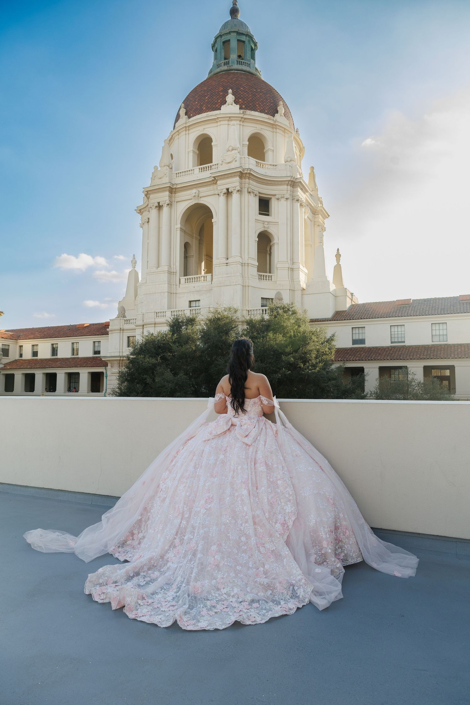 Woman in pink lace ball gown poses before Pasadena City Hall's iconic dome at sunset.