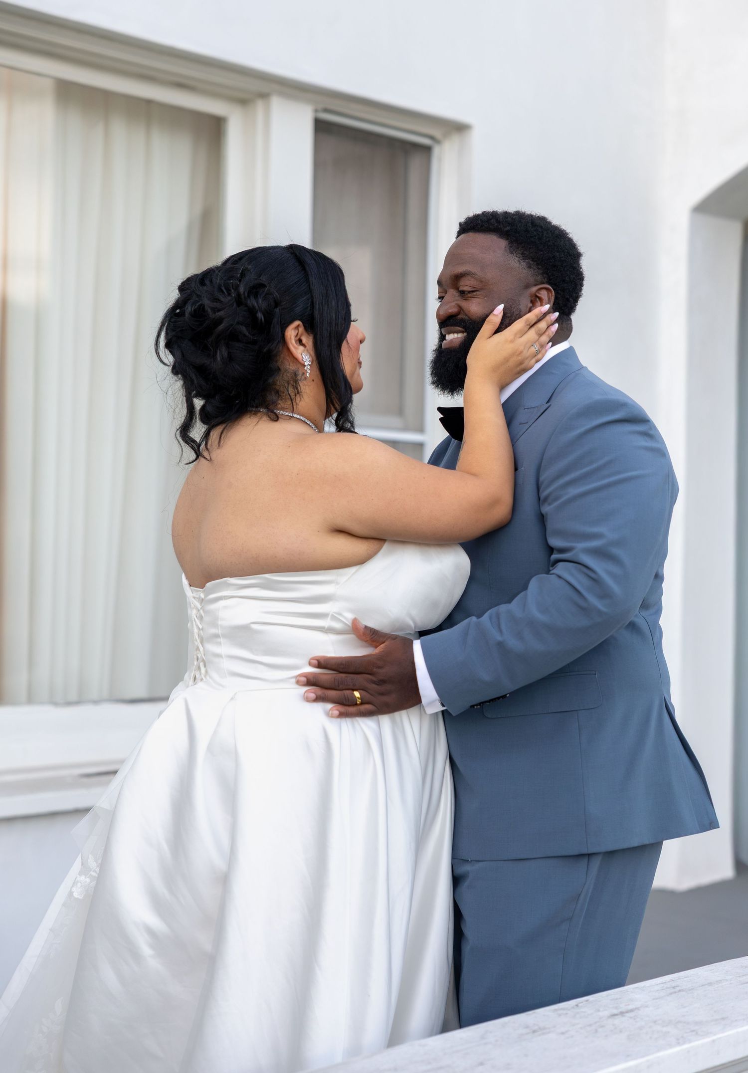 Bride and groom embracing and smiling together on wedding day, groom in blue suit.