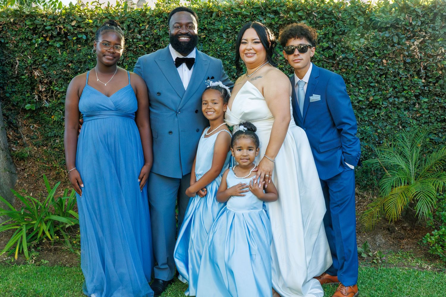 Family of six posing outdoors in coordinating blue formal attire for a special celebration.
