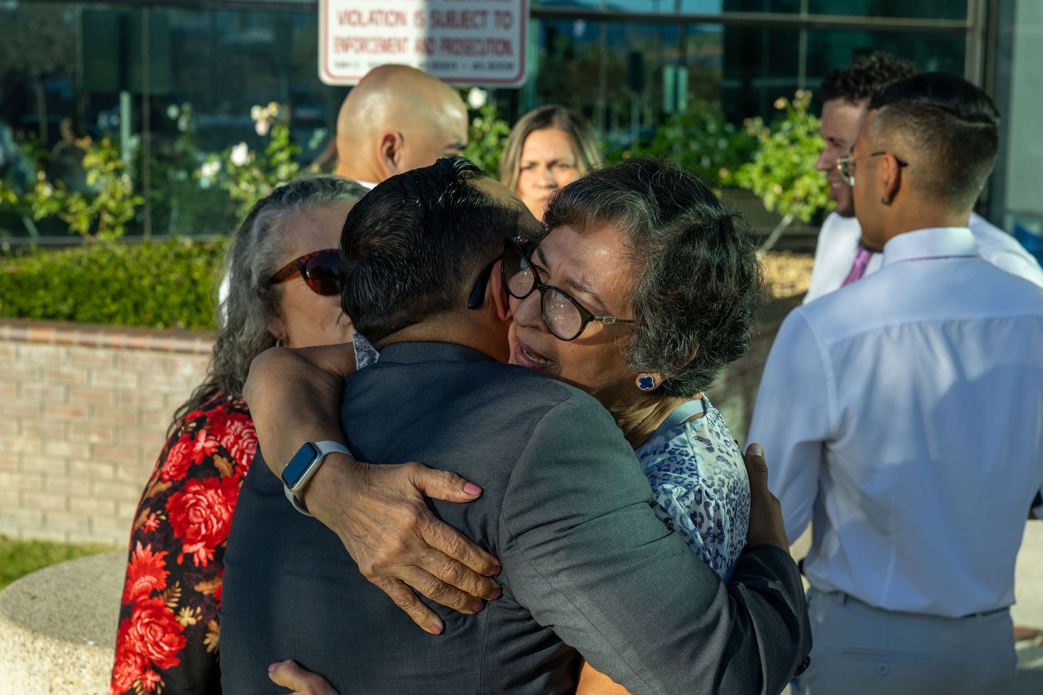 Group of people sharing warm hugs outside a modern building on a sunny day.
