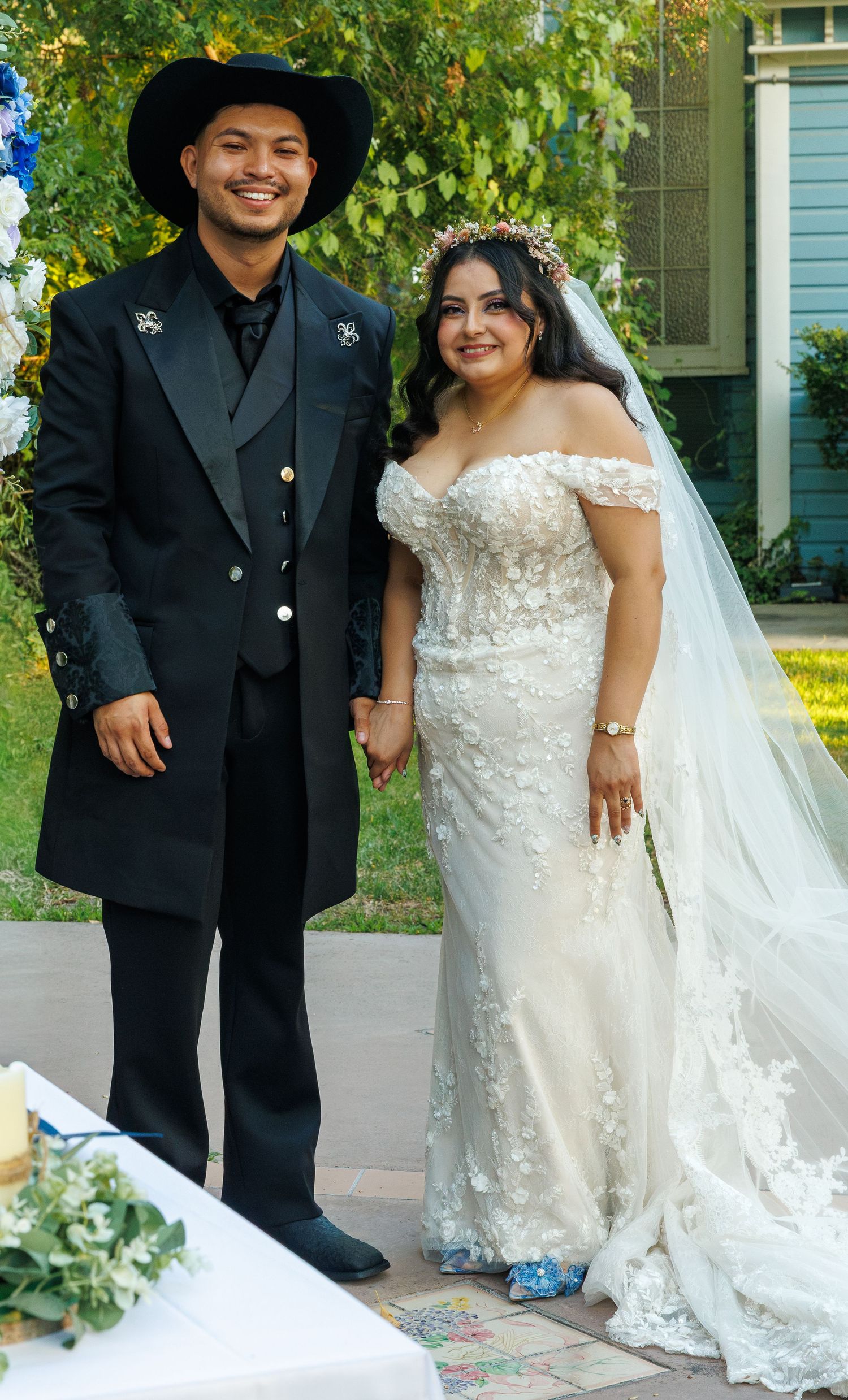 Bride and groom pose together outdoors in elegant wedding attire with cowboy hats.