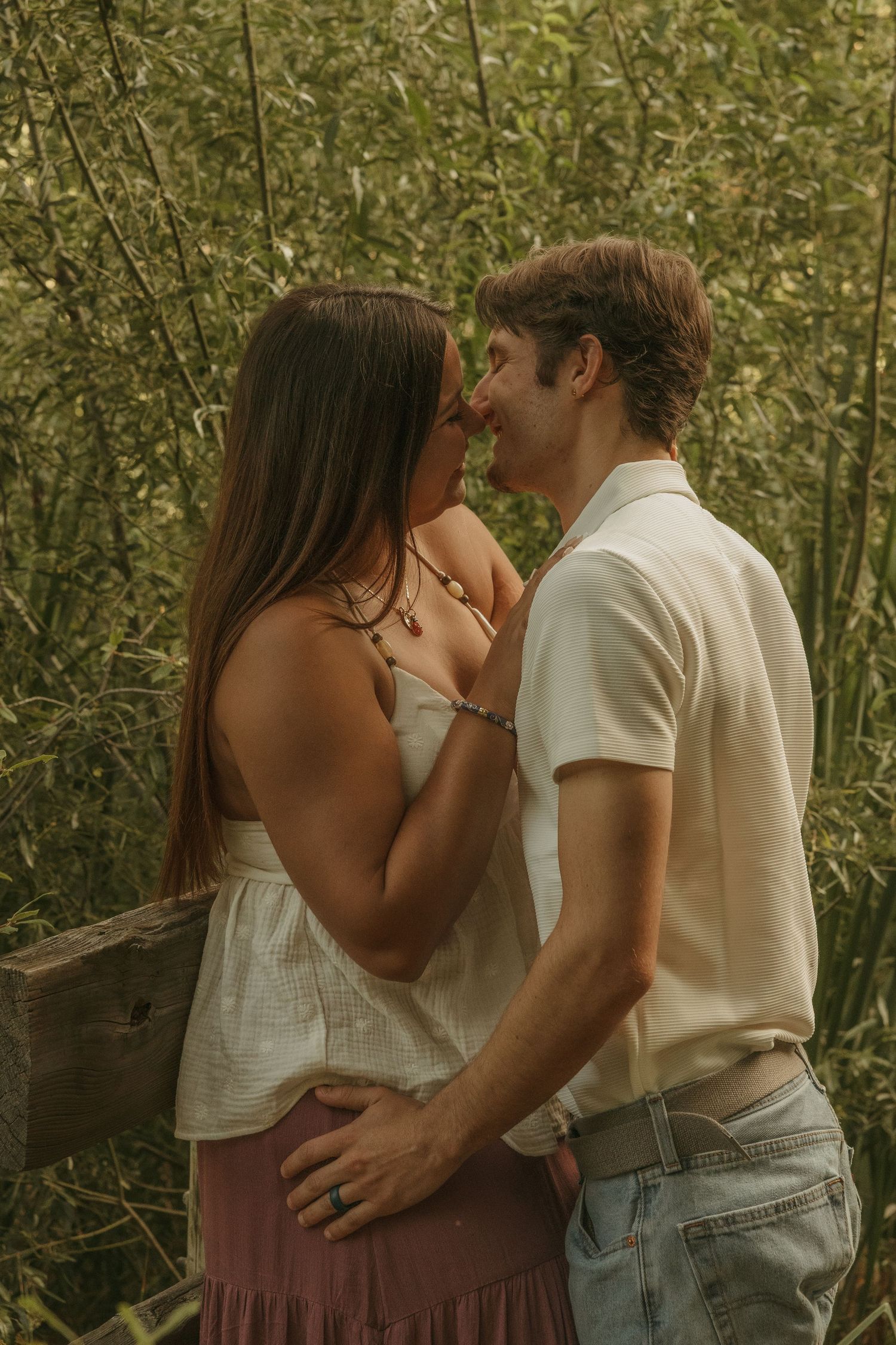 A romantic couple sharing an intimate moment about to kiss surrounded by lush green bamboo in a serene outdoor setting.