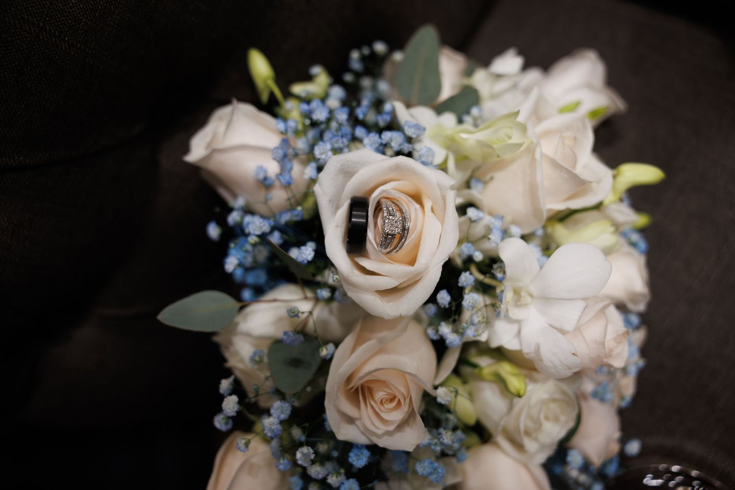 Wedding rings rest on a bridal bouquet of white roses and blue forget-me-nots.
