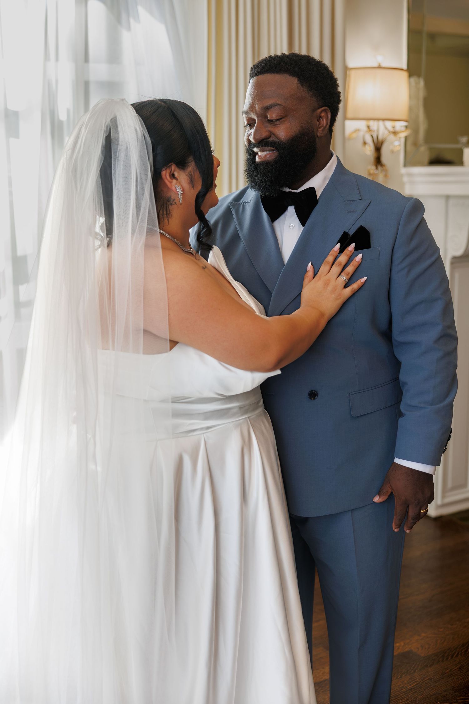 Bride in white gown and veil sharing emotional first look moment with groom in blue suit.