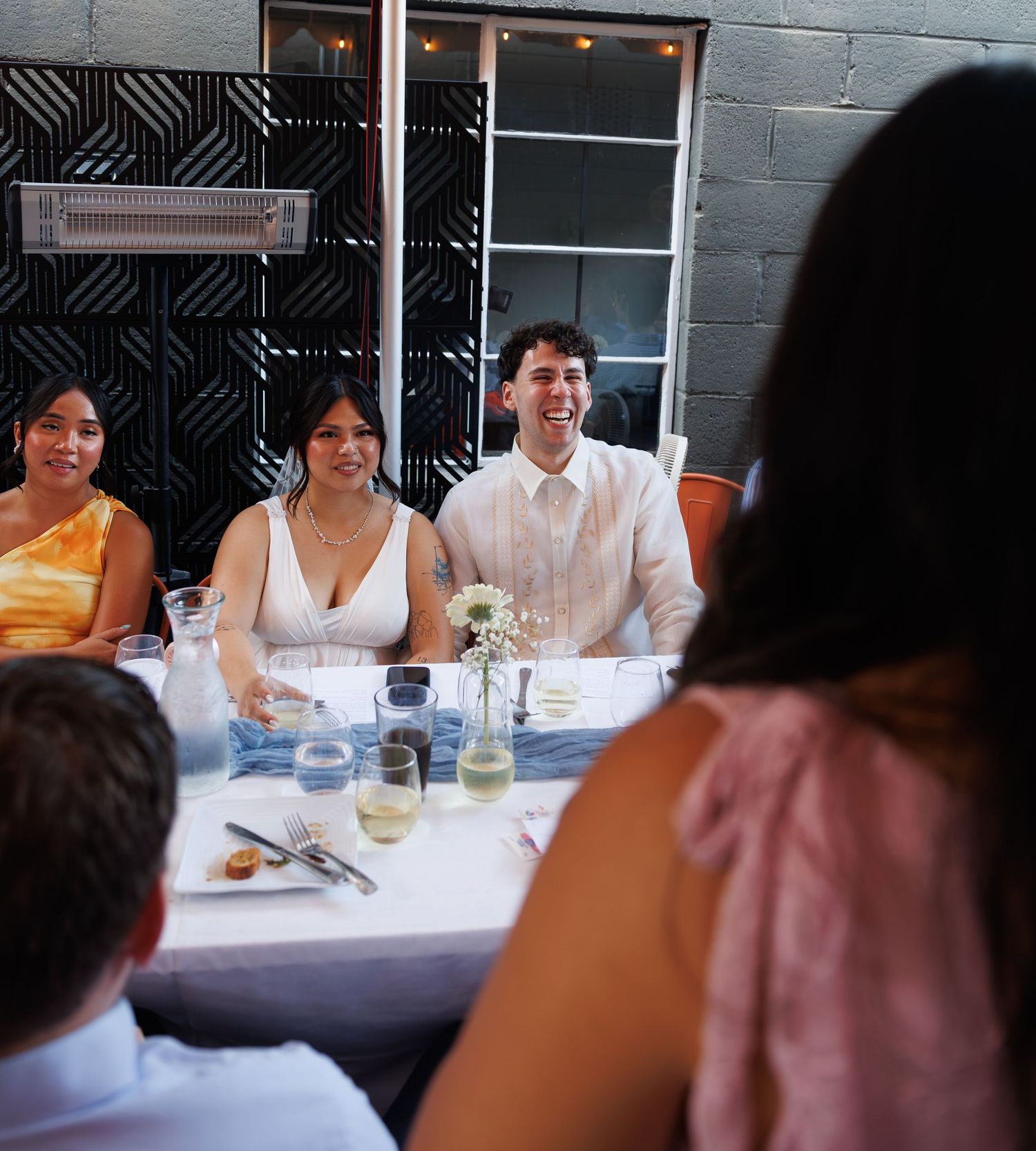 Bride and groom laughing at wedding reception dinner table with guests in elegant venue.