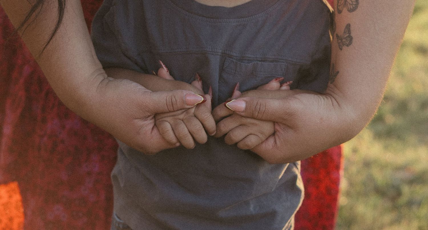 A mother tenderly holds her toddlers tiny hands together in a touching outdoor moment.